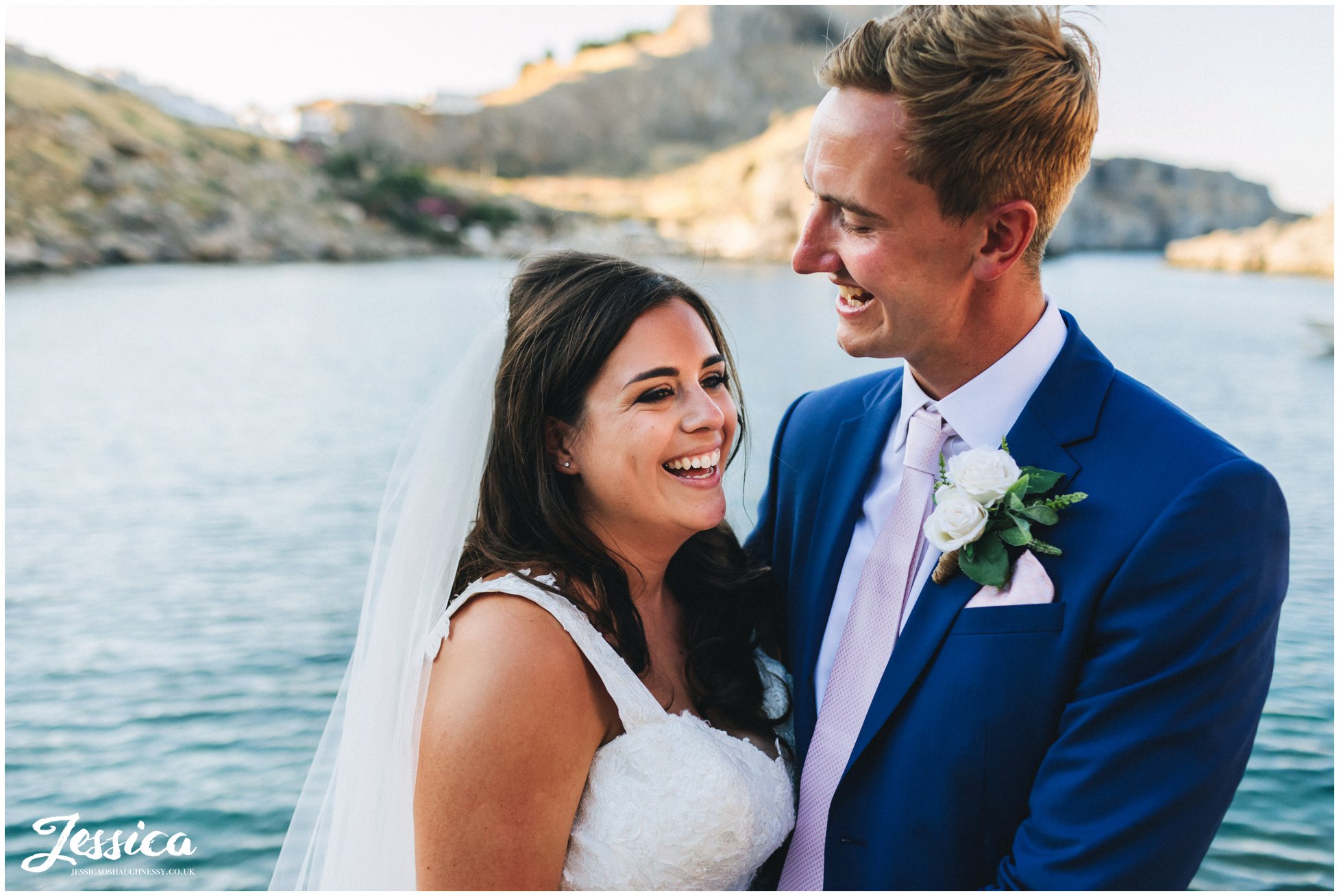 bride & groom laughing with the sea in the background on their destination wedding day in greece