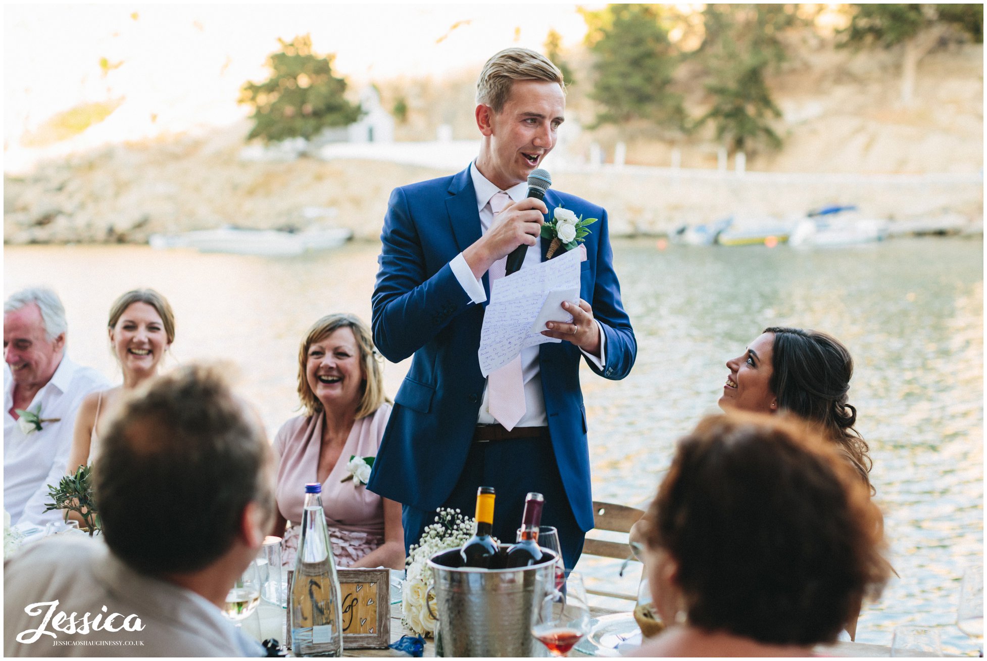 groom gives his speech with the sea in the background