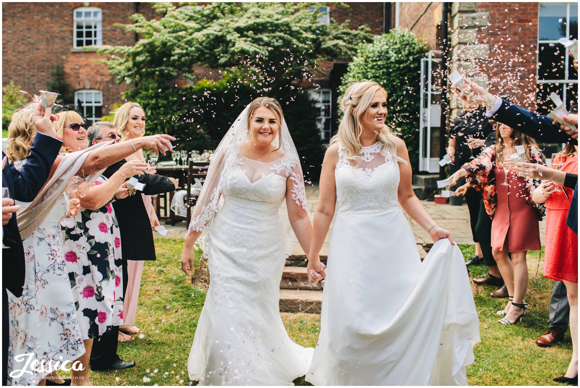 guests throw confetti over the brides as they walk through