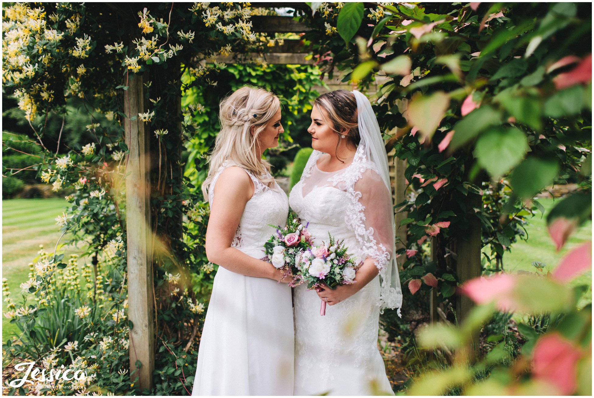 the newly wed's stand together under the arch way in mottram hall's gardens