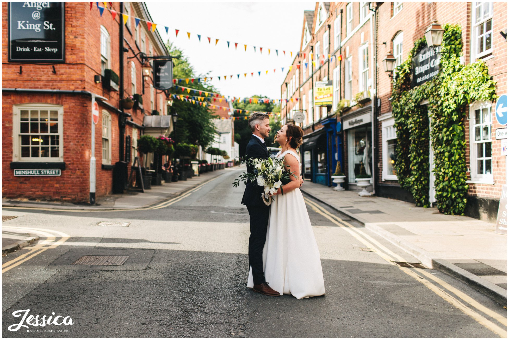 the newly wed's kiss in the middle of the road decorated with bunting
