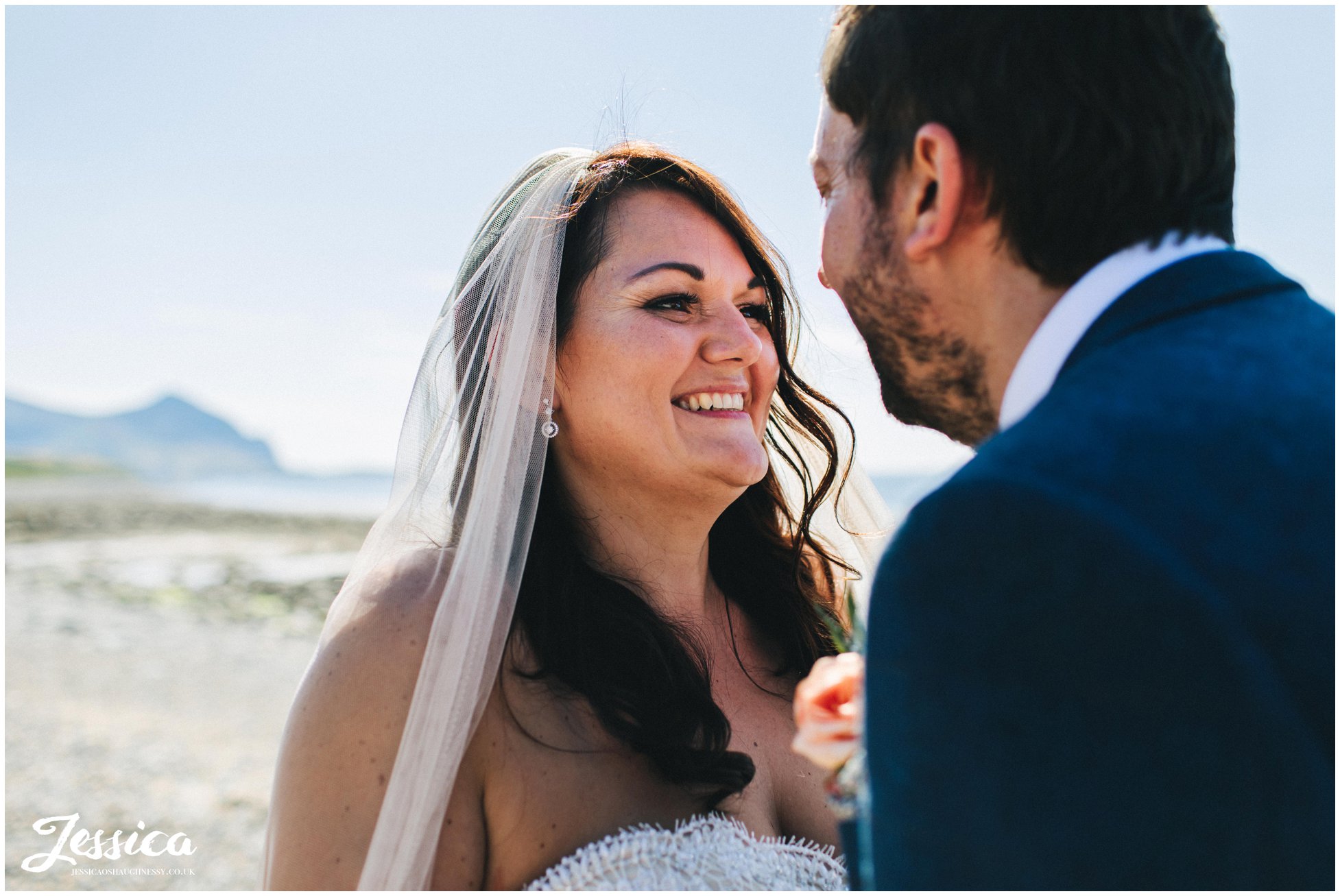 the bride smiles to her groom with the sea behind them