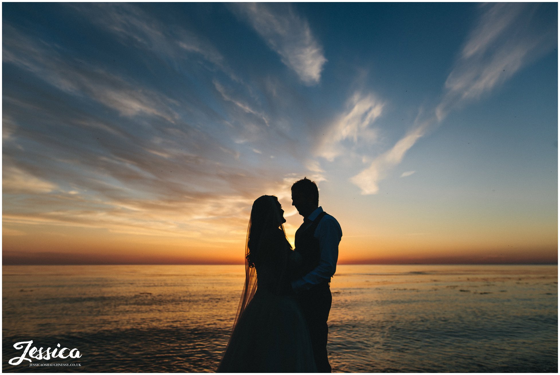 bride & groom stand in front of epic sun set in north wales