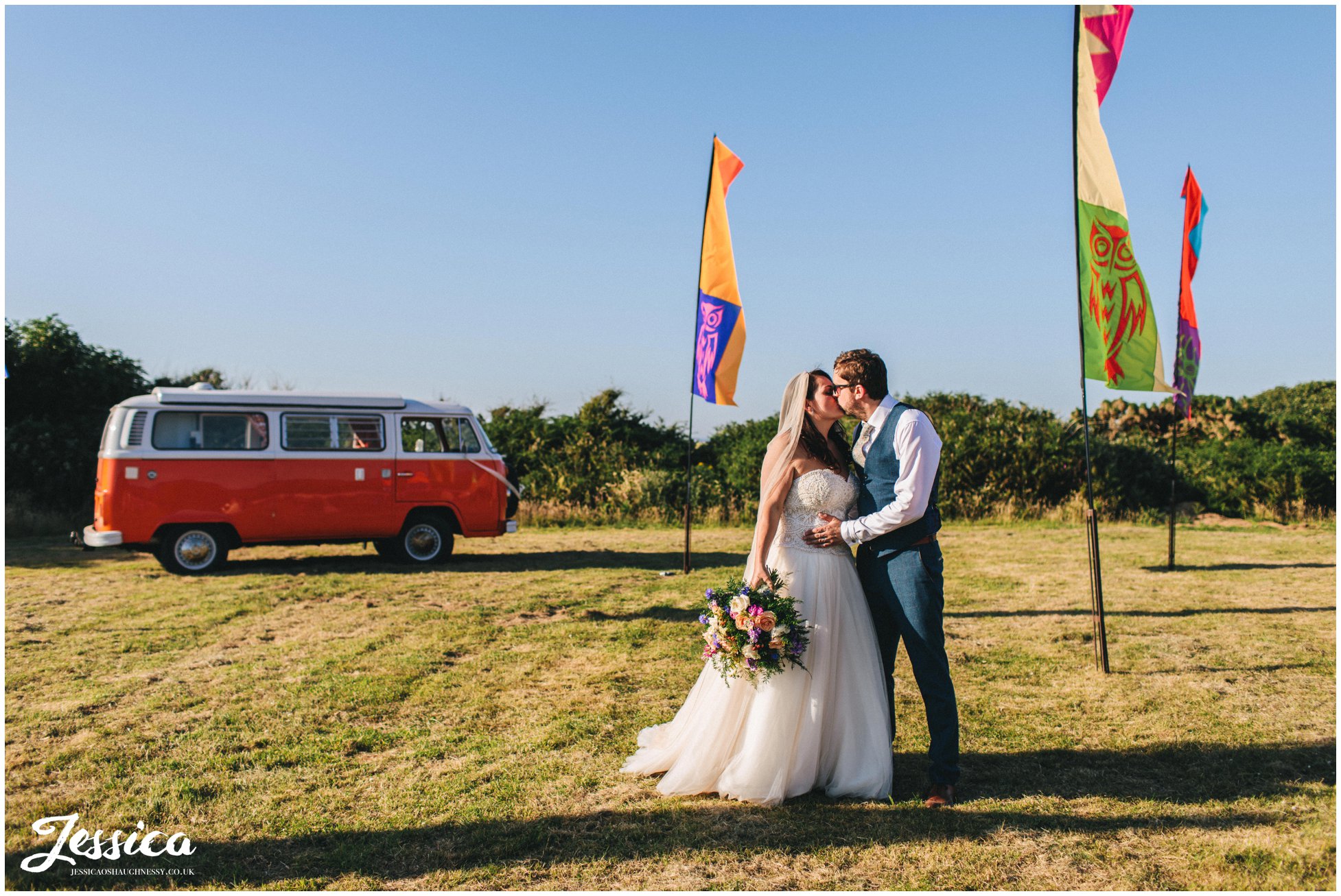 newly wed's kiss in front of vw camper and festival flags