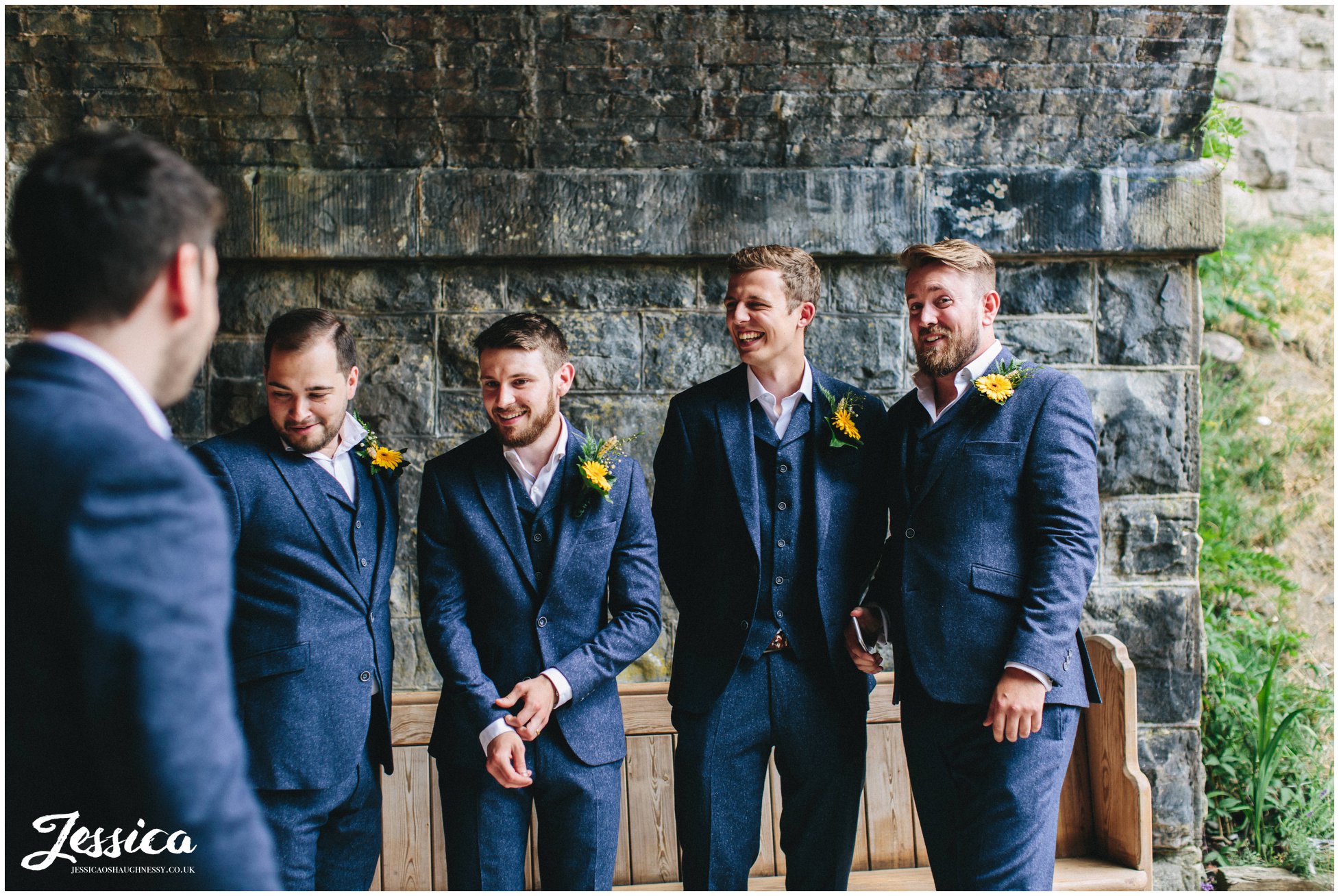 groomsmen laugh as they wait under the bridge