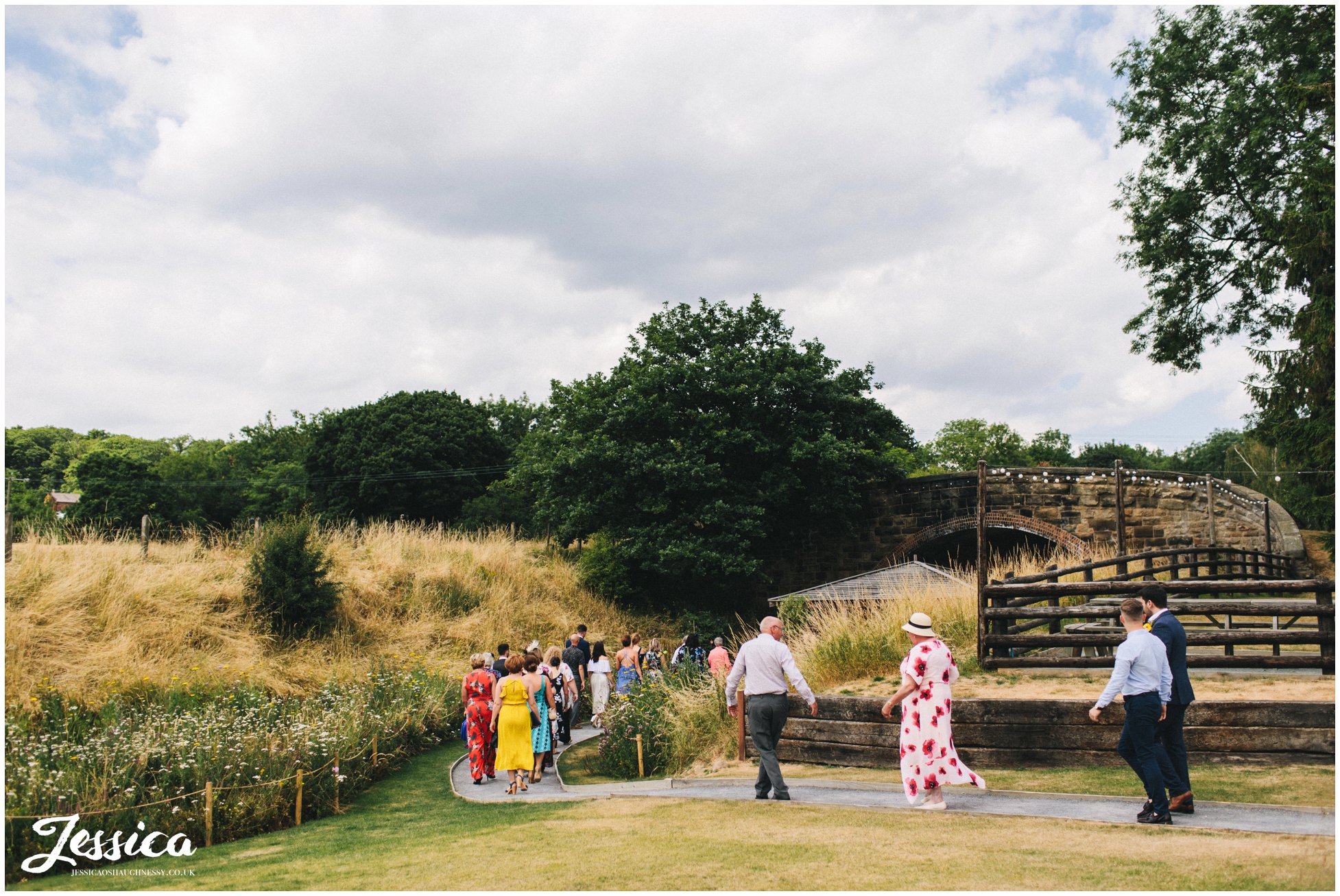 guests walk down the wildflower lined path to the bridge