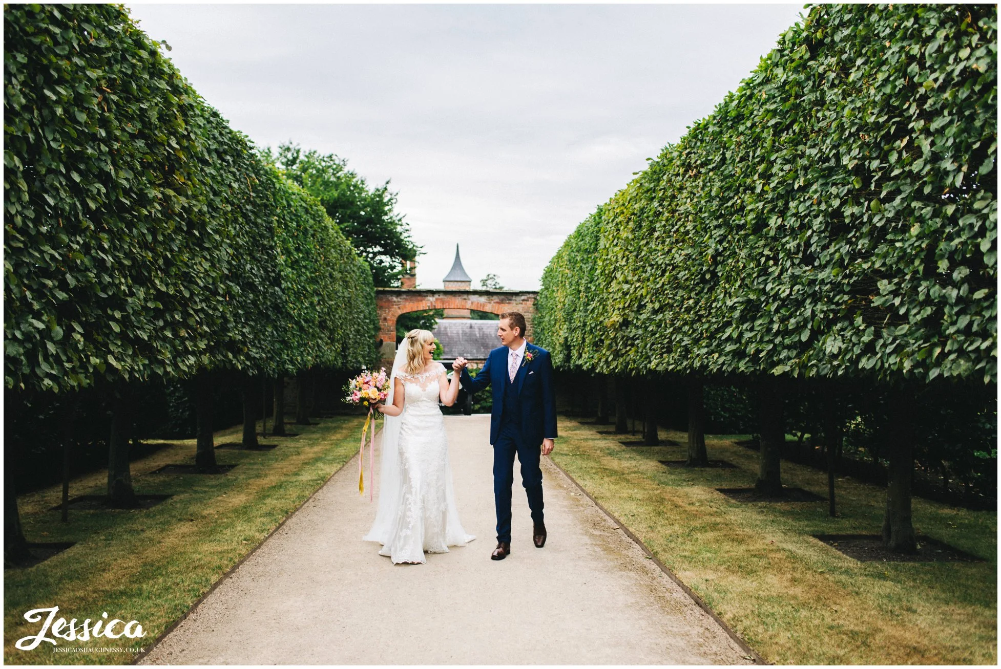 newlywed's walk through the tree lined path holding hands