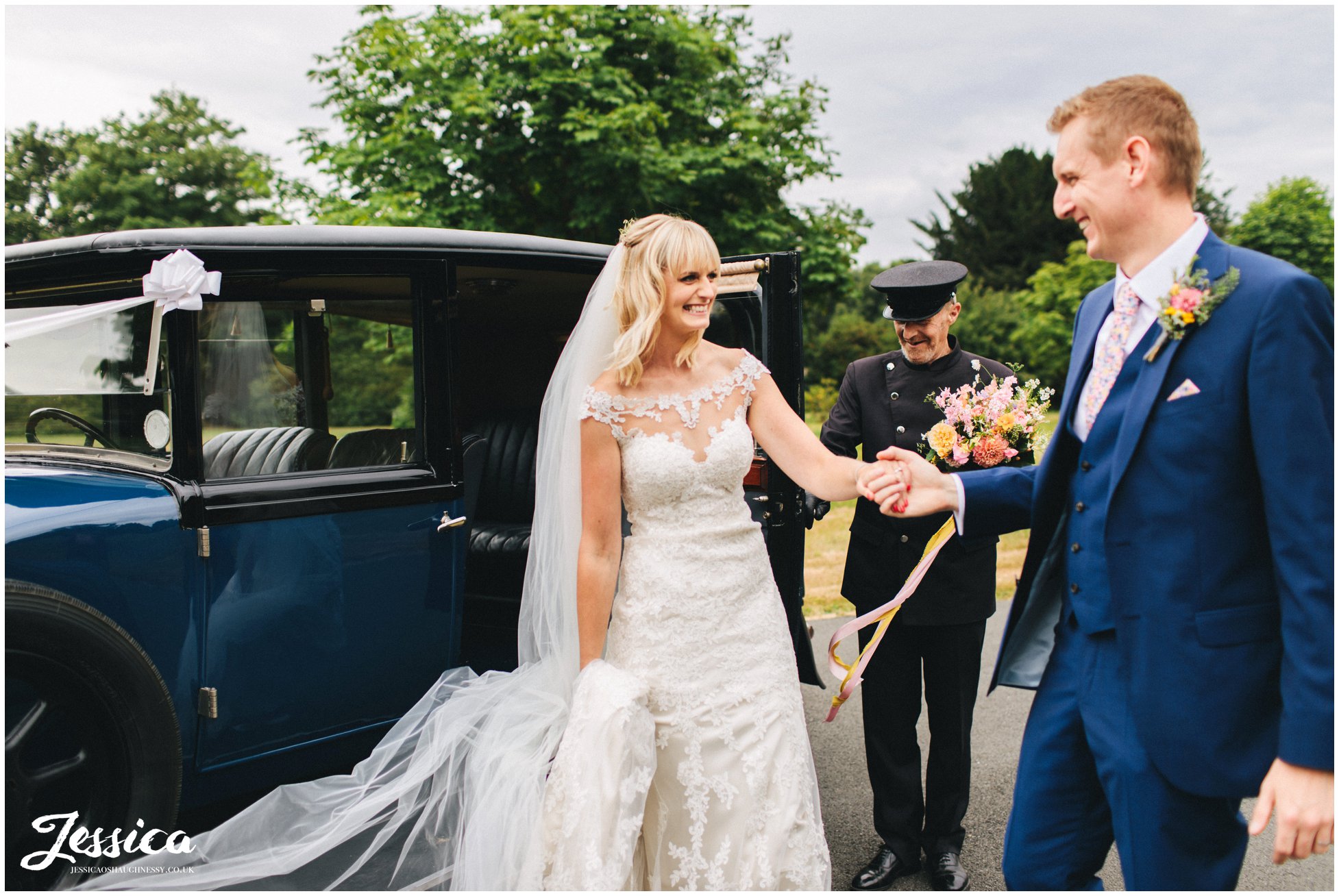 the groom helps his bride out of the wedding car