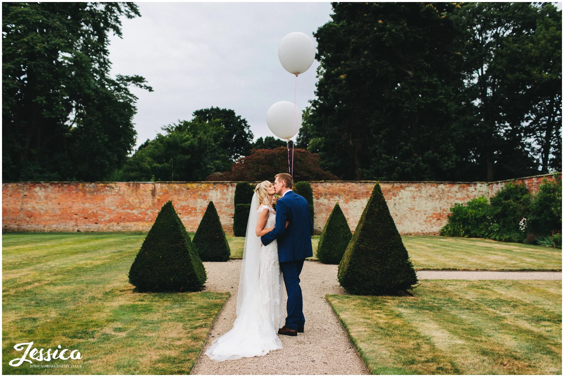 couple kiss in combermere abbey grounds holding balloons