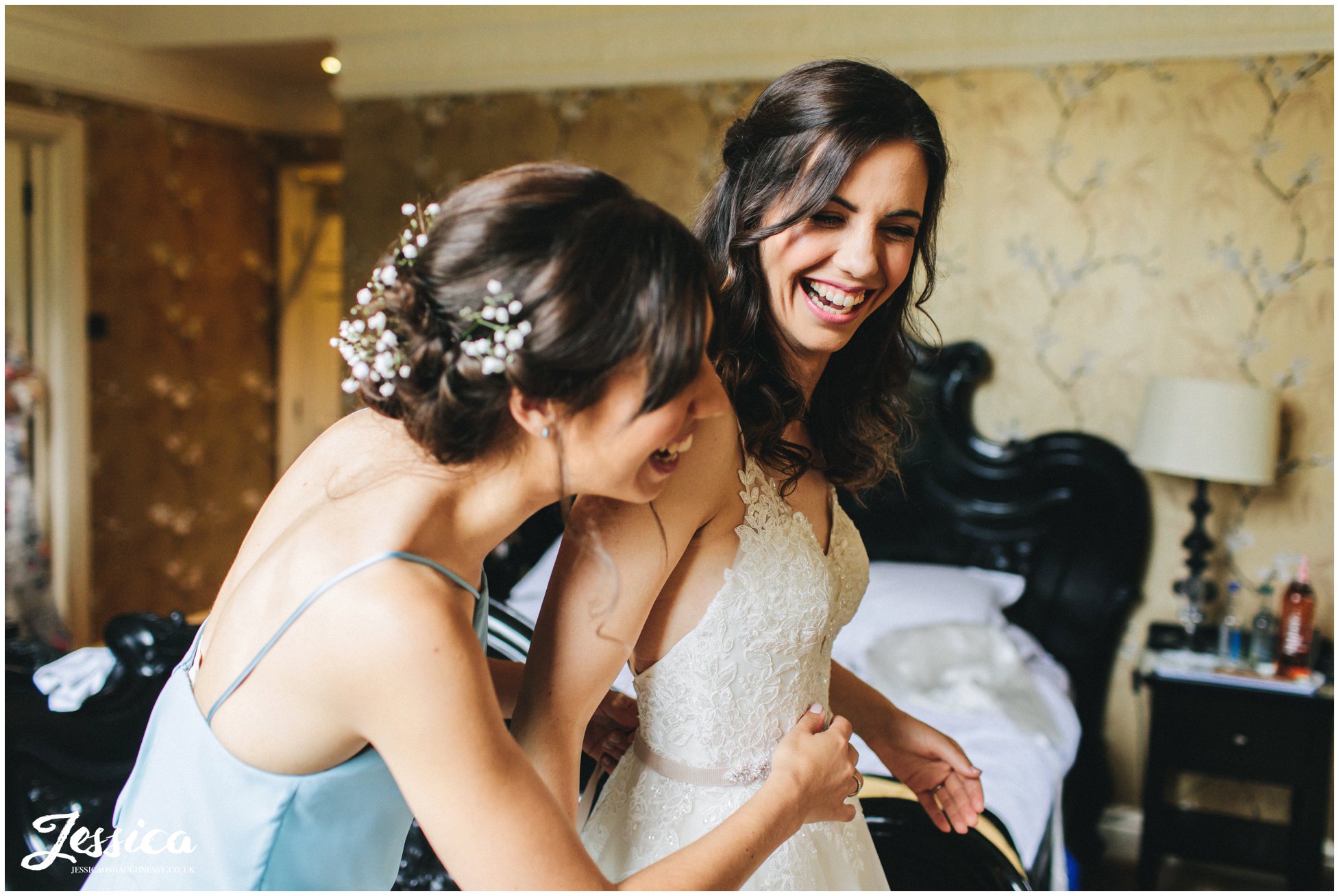 bride laughs with her sister as she gets into wedding dress