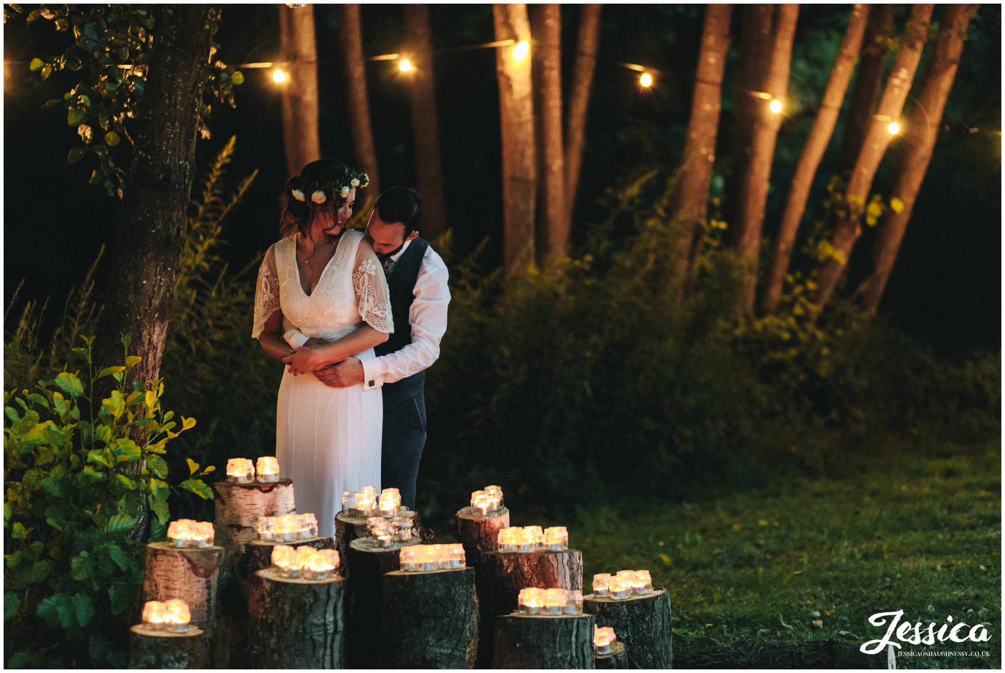 newly wed's embrace in front of lit candles as the sun goes down
