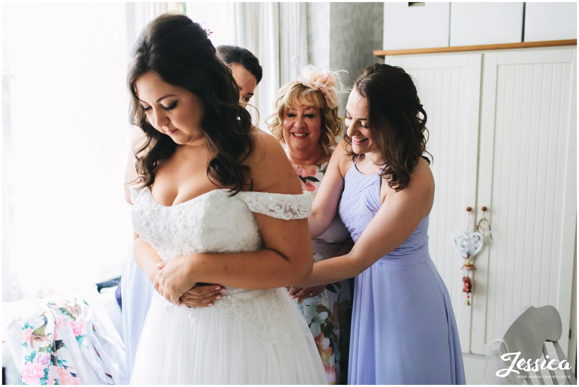 the brides mother & sisters help her into her wedding dress