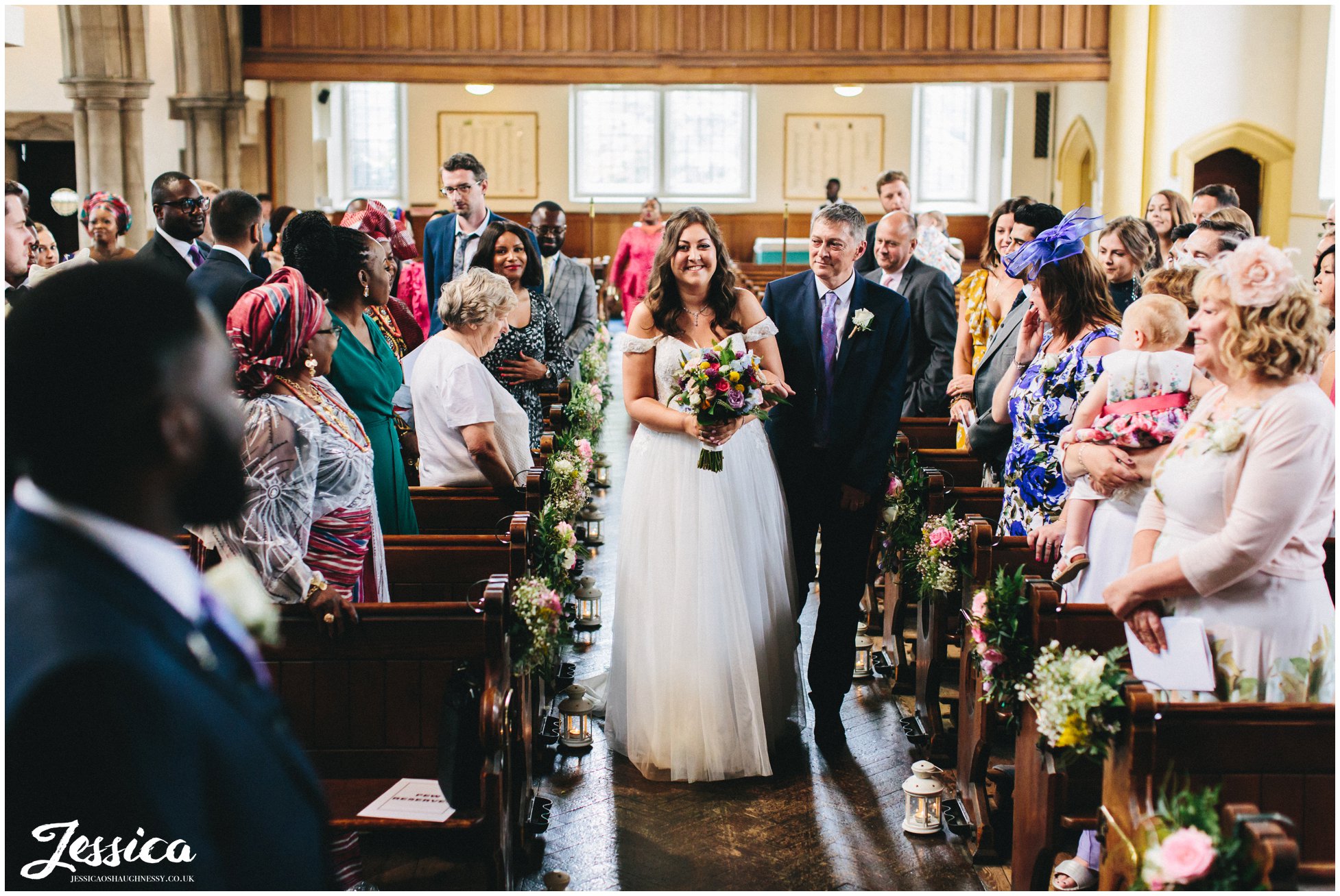 the bride smiles at her groom as she walks down the aisle with her dad