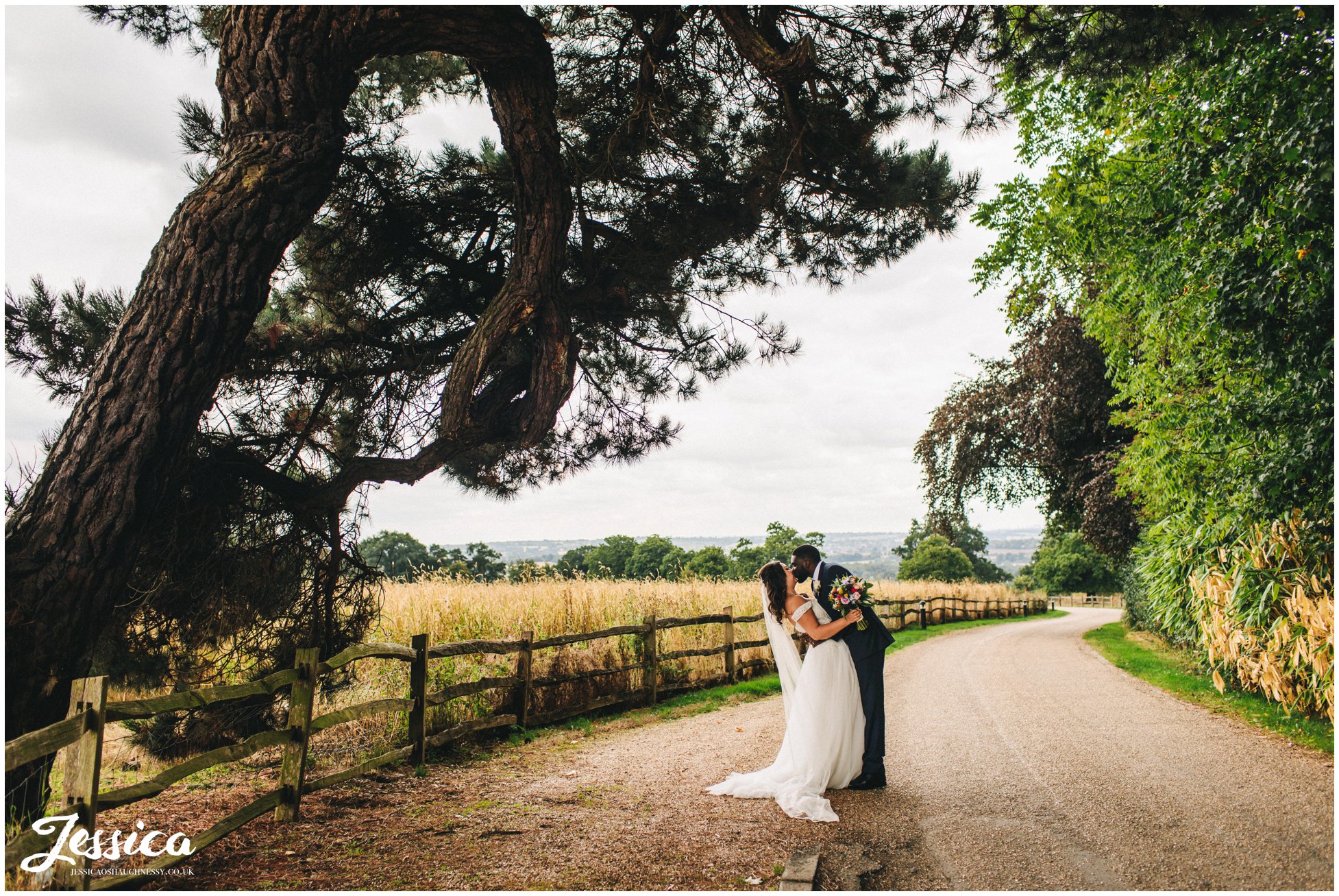 husband and wife kiss under a huge tree on gaynes park driveway