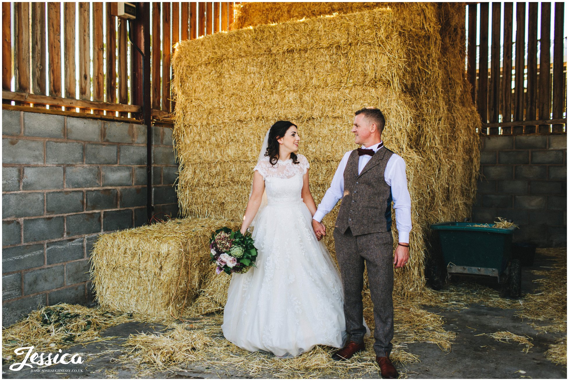 newly wed's hold hands in front of hay bales