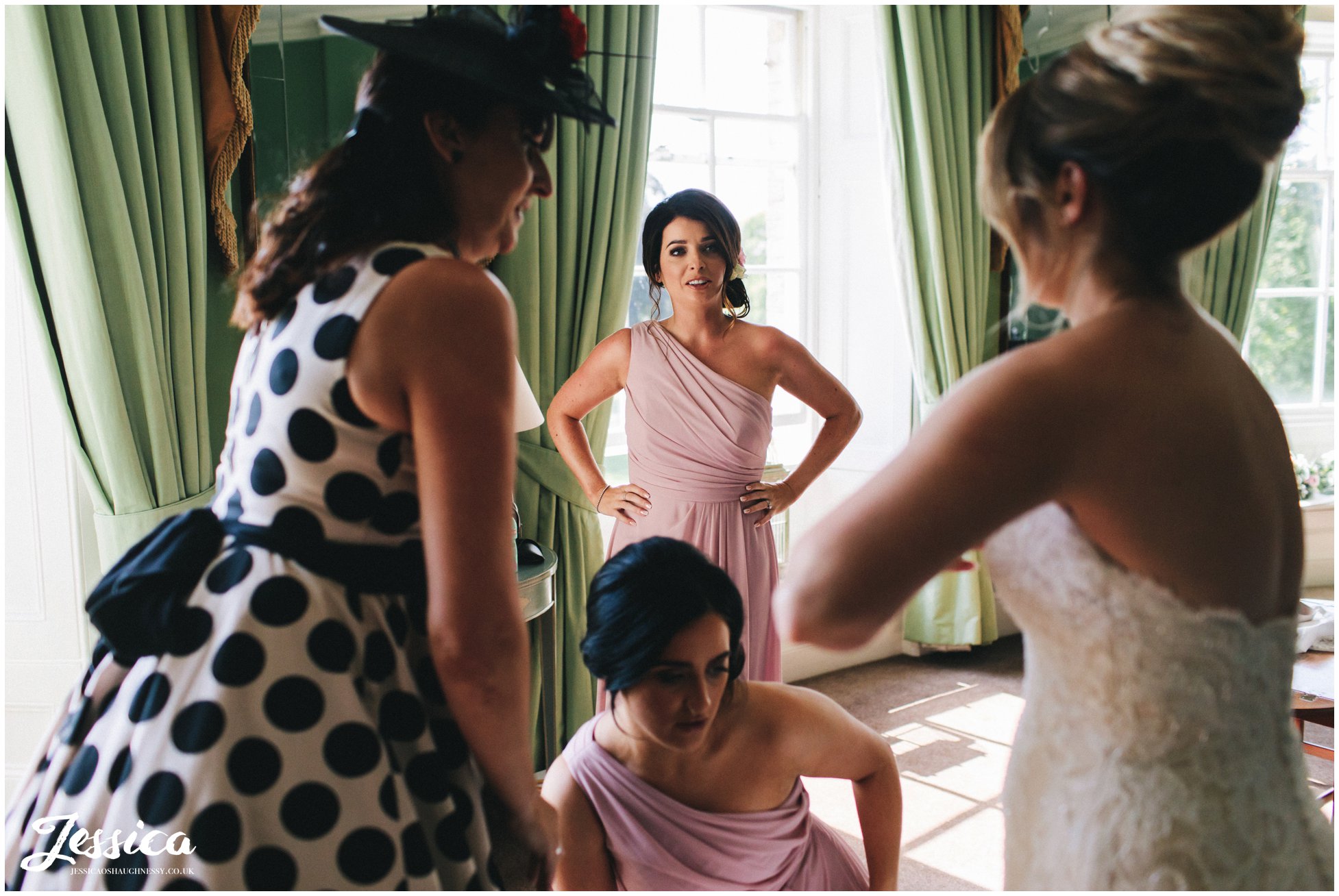 bridesmaids admire the bride as she gets into her dress