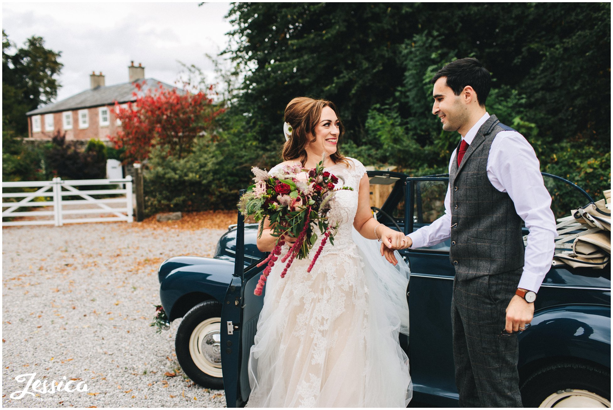 groom helps his bride out of the vintage wedding car