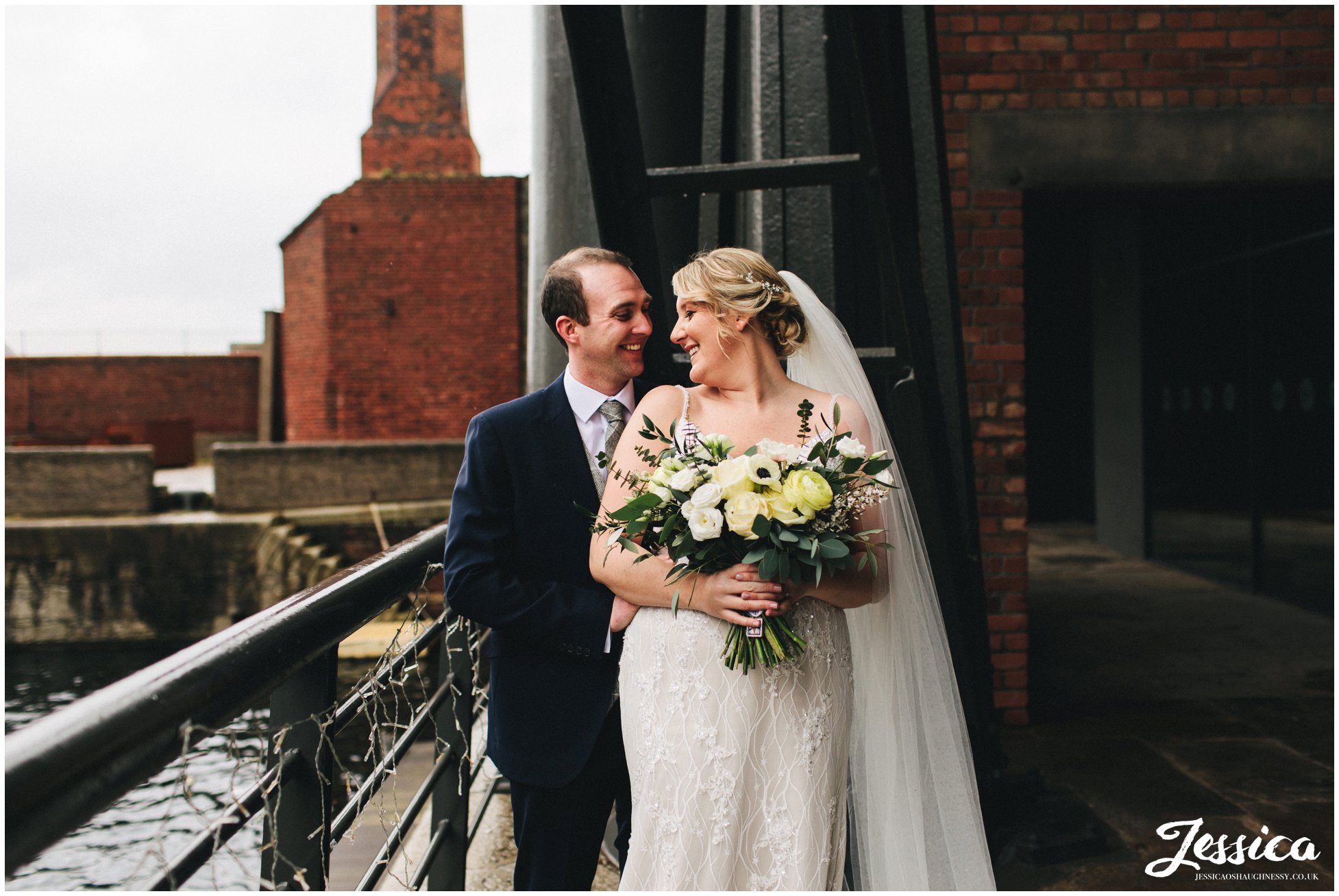 the bride &amp; groom embrace along side liverpool docks