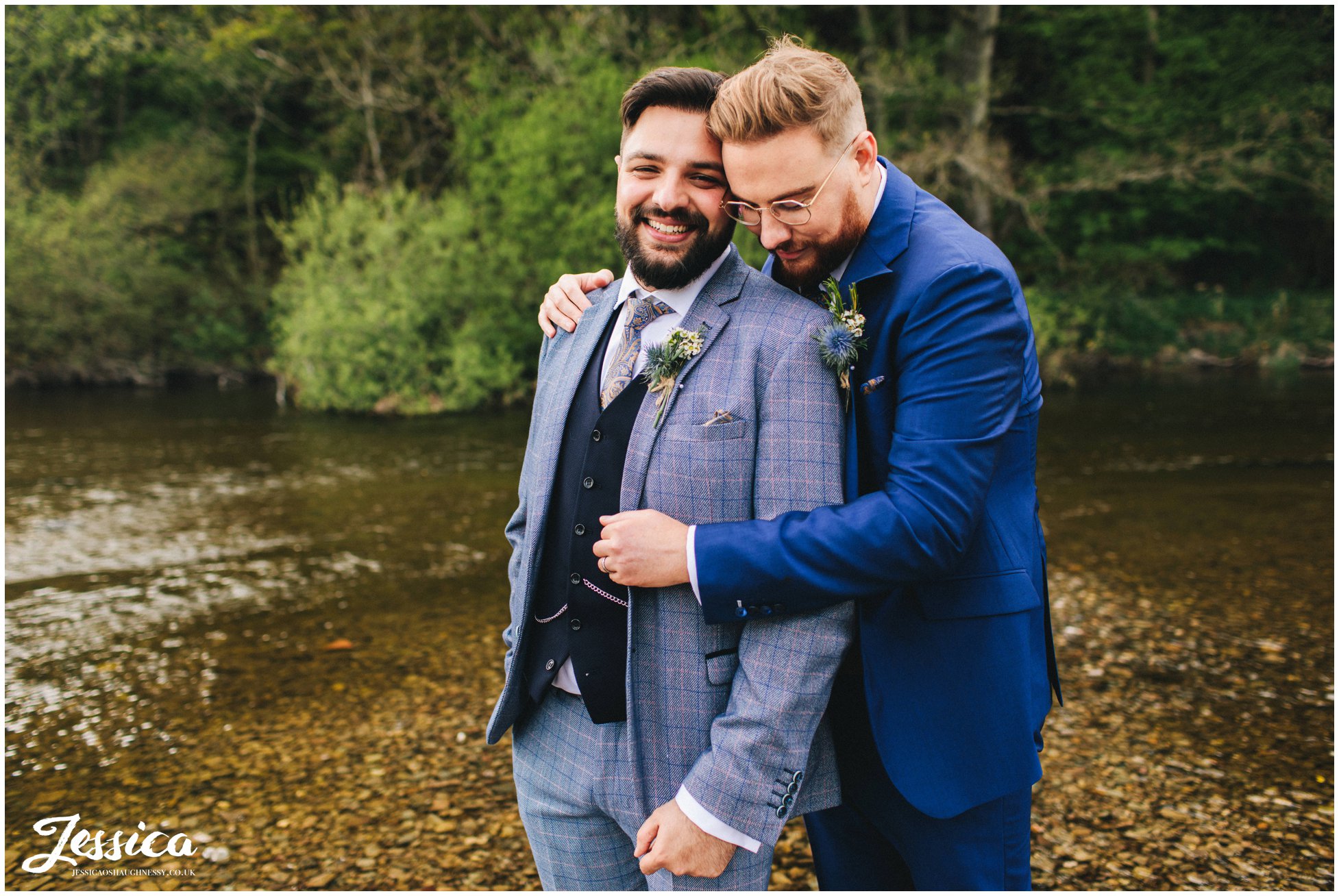 the couple embrace by the river at their lake district wedding