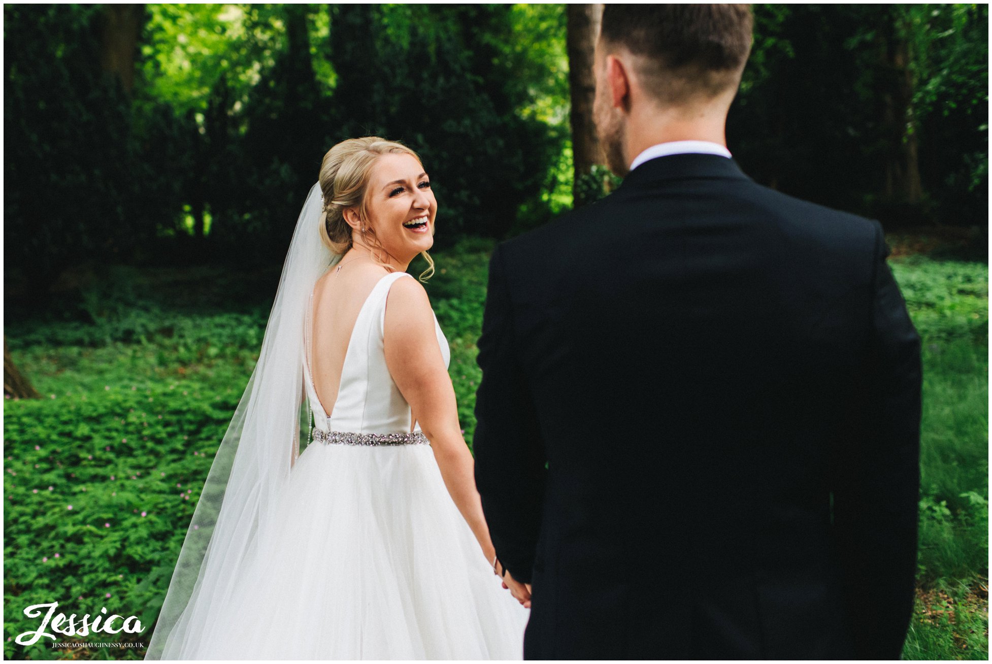 the bride holds grooms hand as she walks through the trees