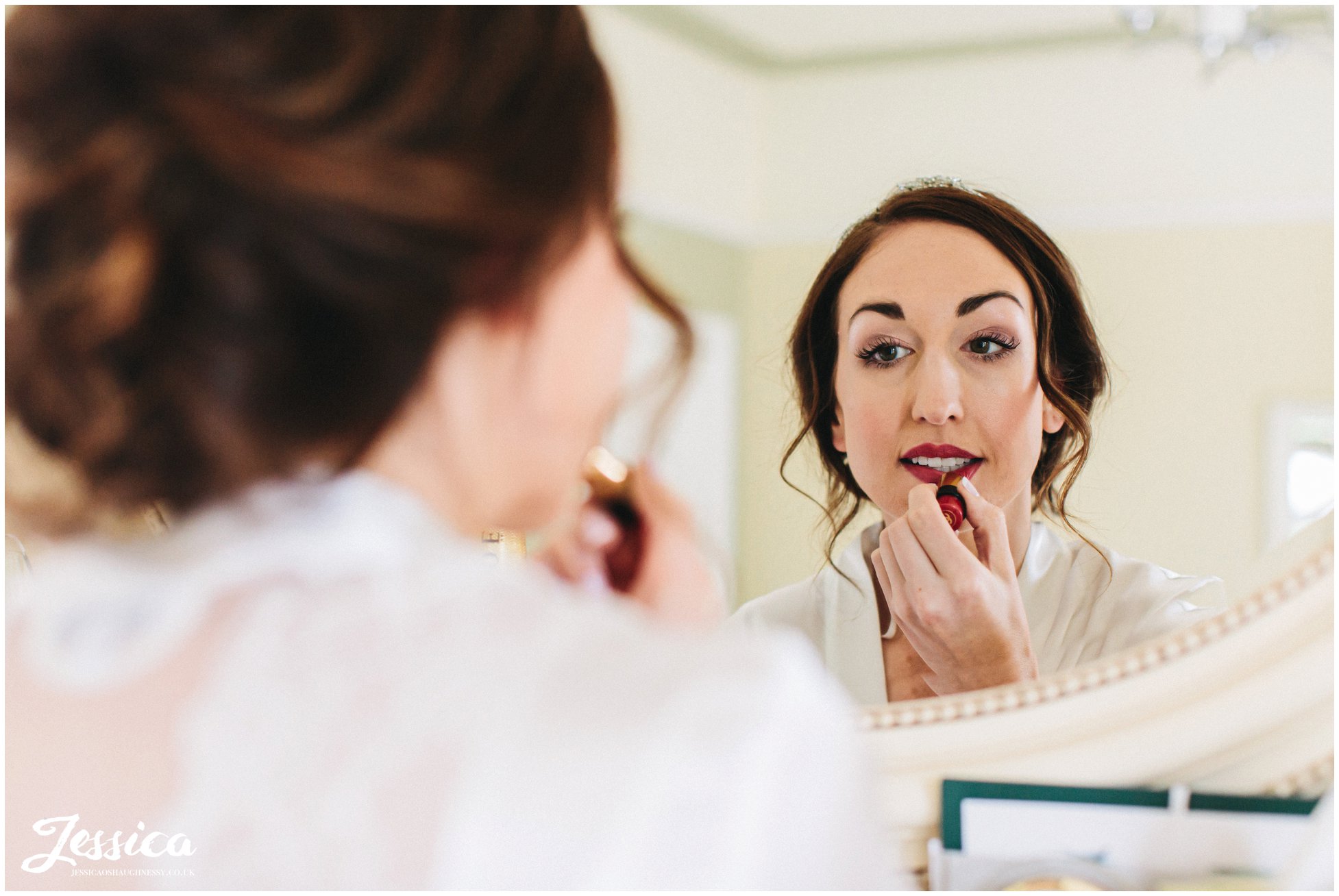 the bride applies red lipstick in the mirror