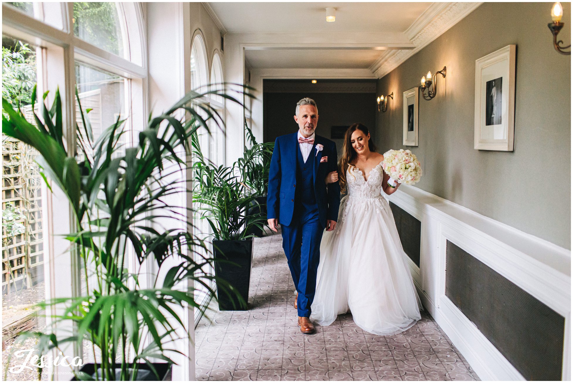 bride &amp; father walk down mottram hall corridor to the ceremony