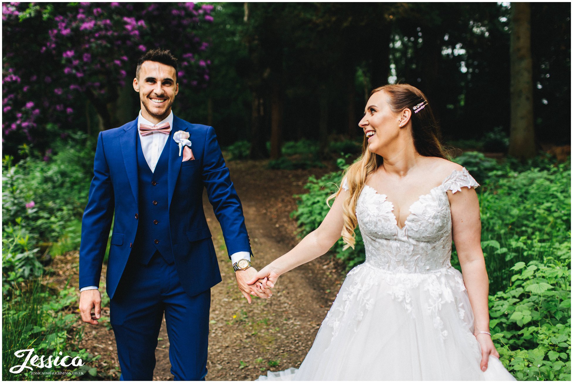 bride takes grooms hand as they walk through the woods
