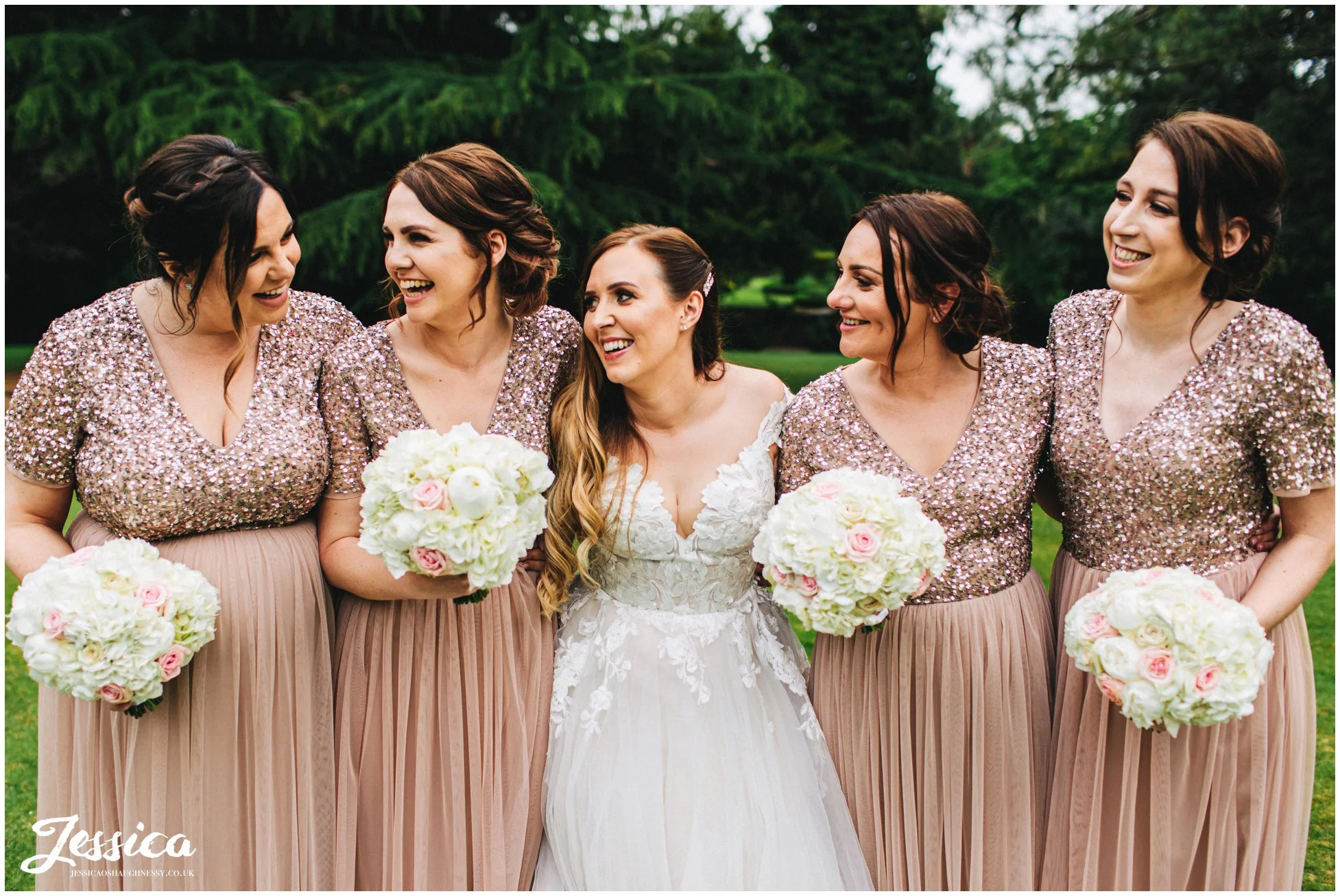 bride & bridesmaids laugh together in the venue gardens
