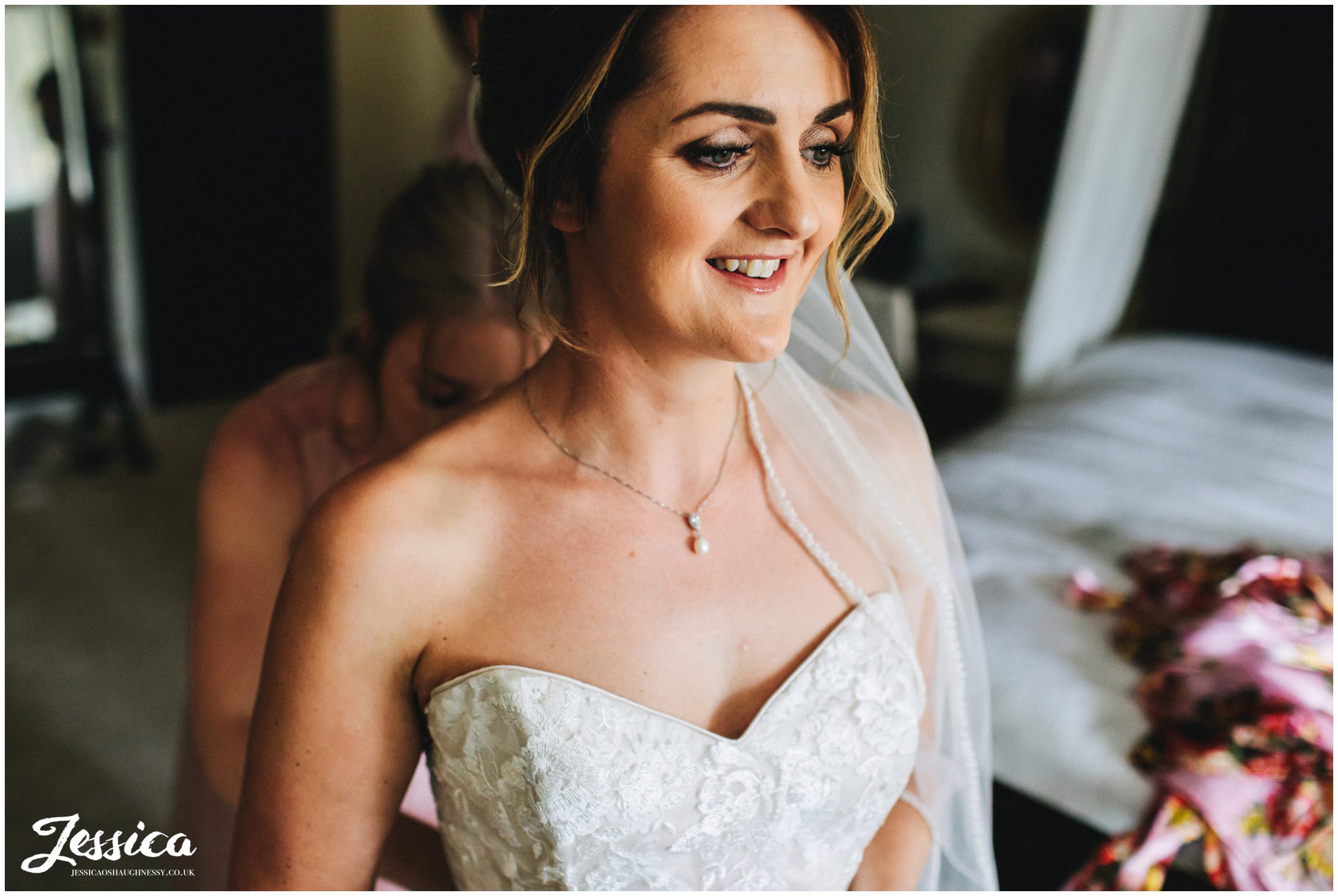 bride smiles as her dress is fastened by her bridesmaids