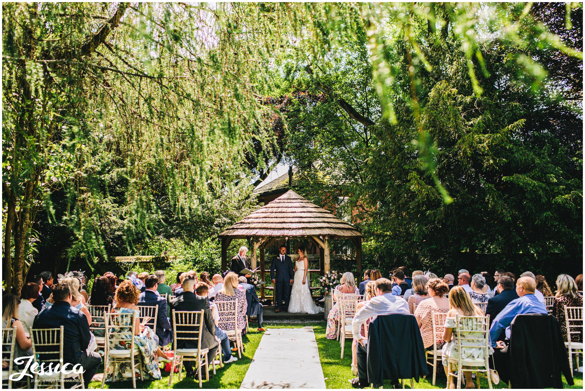 bride &amp; groom stand under floral structure for their outdoor wedding at eyam hall in derbyshire