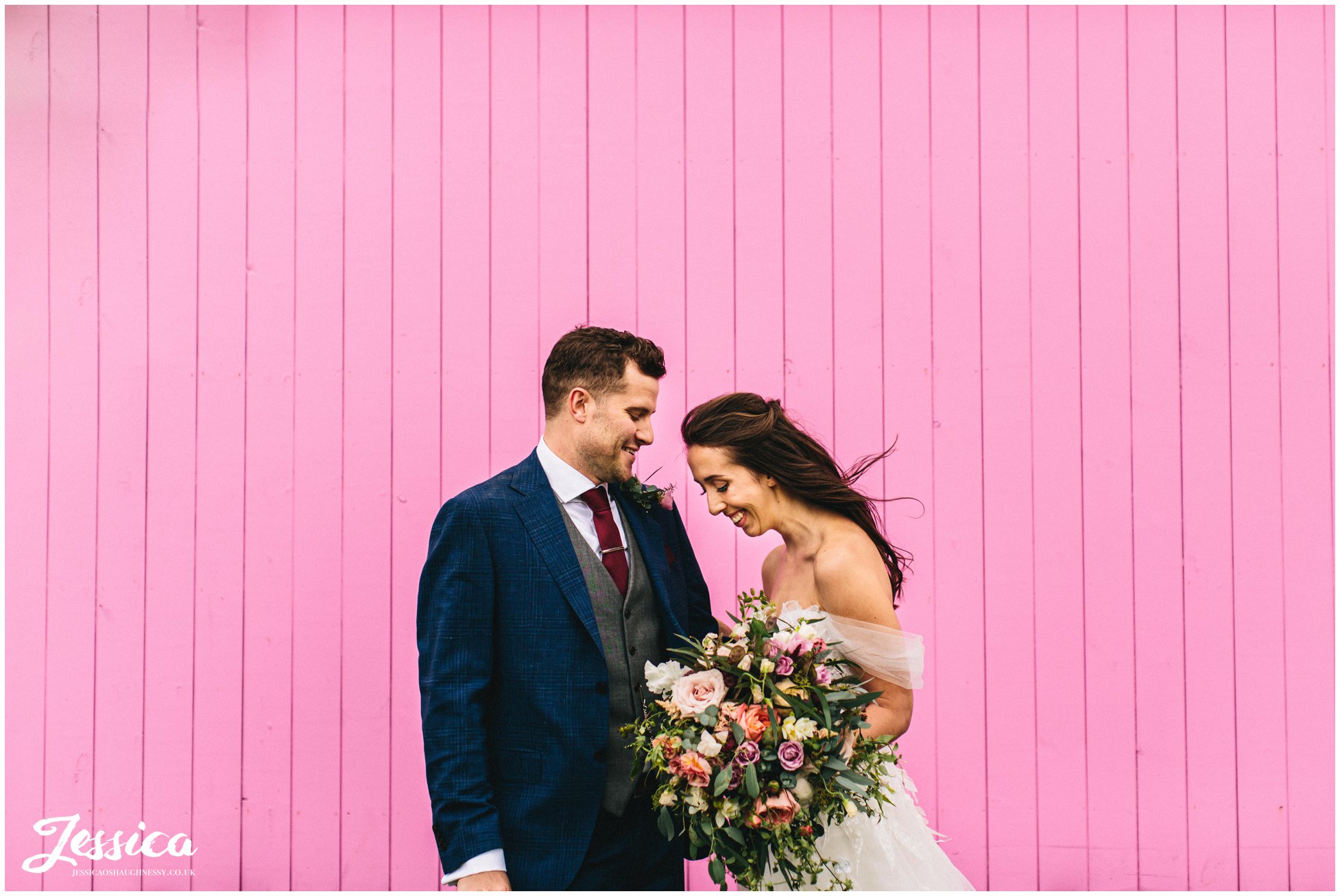 the bride &amp; groom stand in front of the pink shepherds hut colourful wedding photography