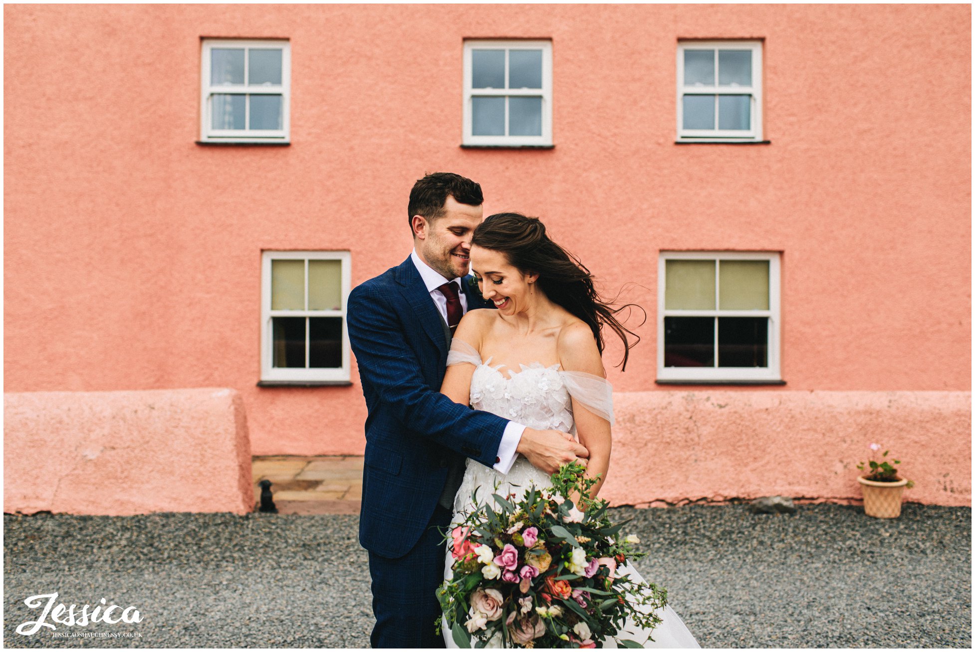 newly wed's have photographs in front of the pink farm house in anglesey