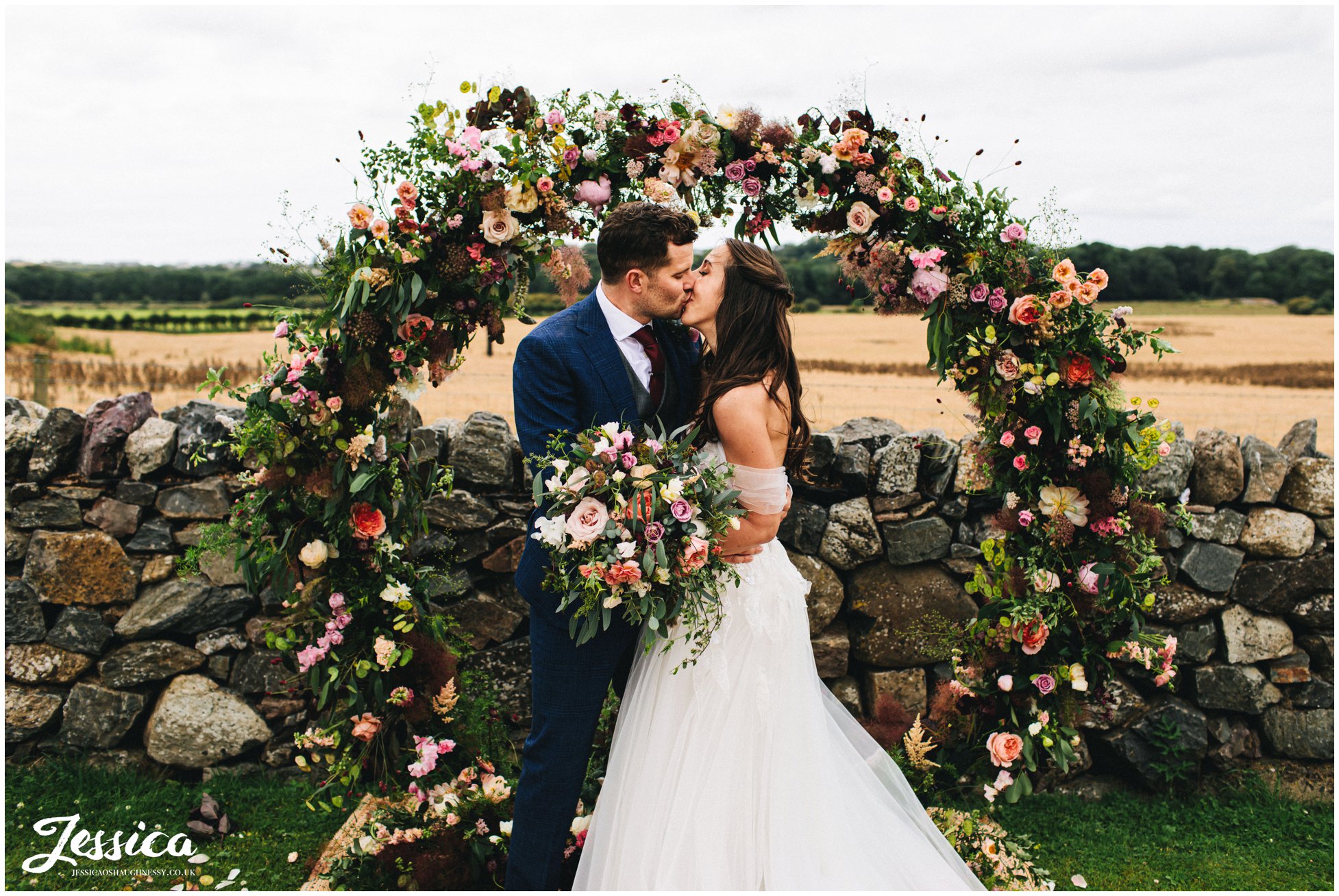 bride & groom kiss in front of floral arch