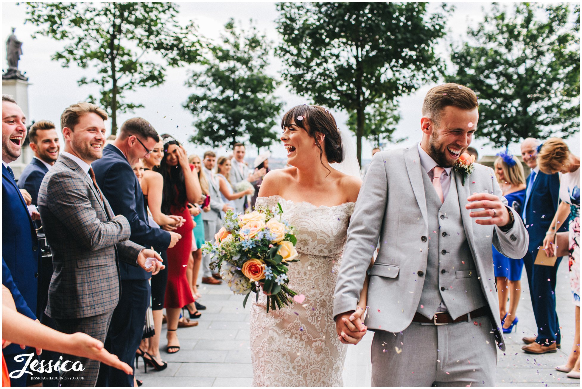 the bride and groom walk through confetti line outside the liver building