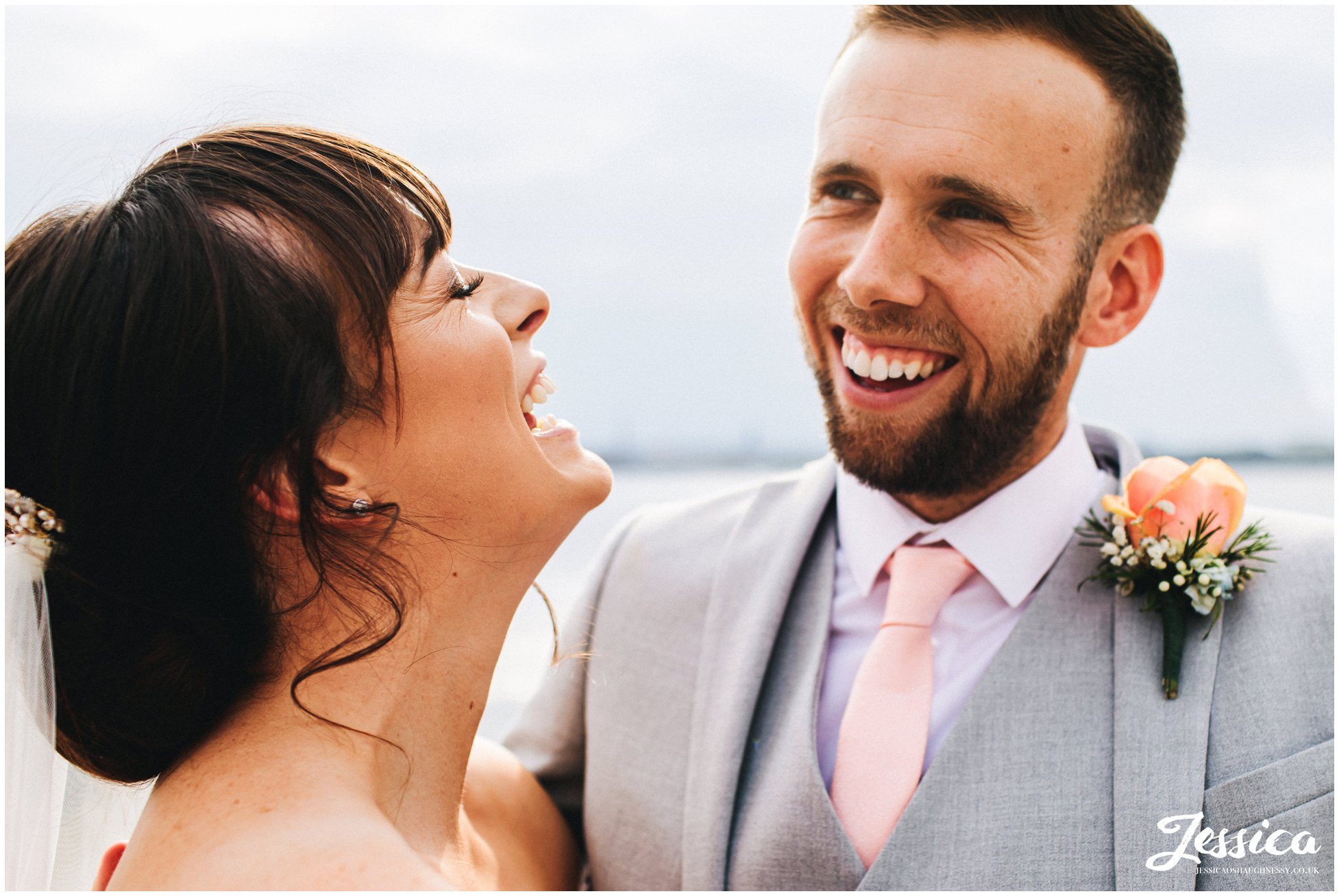 bride &amp; groom laugh with each other on the waterfront