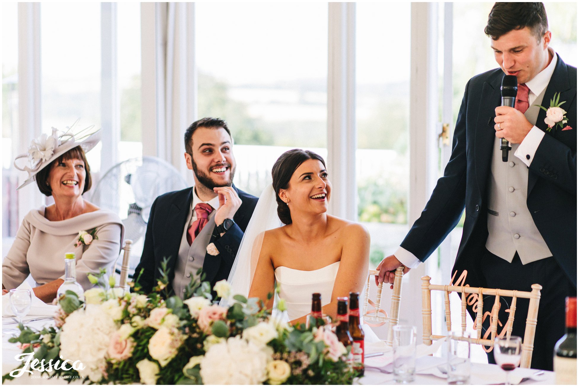 bride laughs as her husband delivers his speech