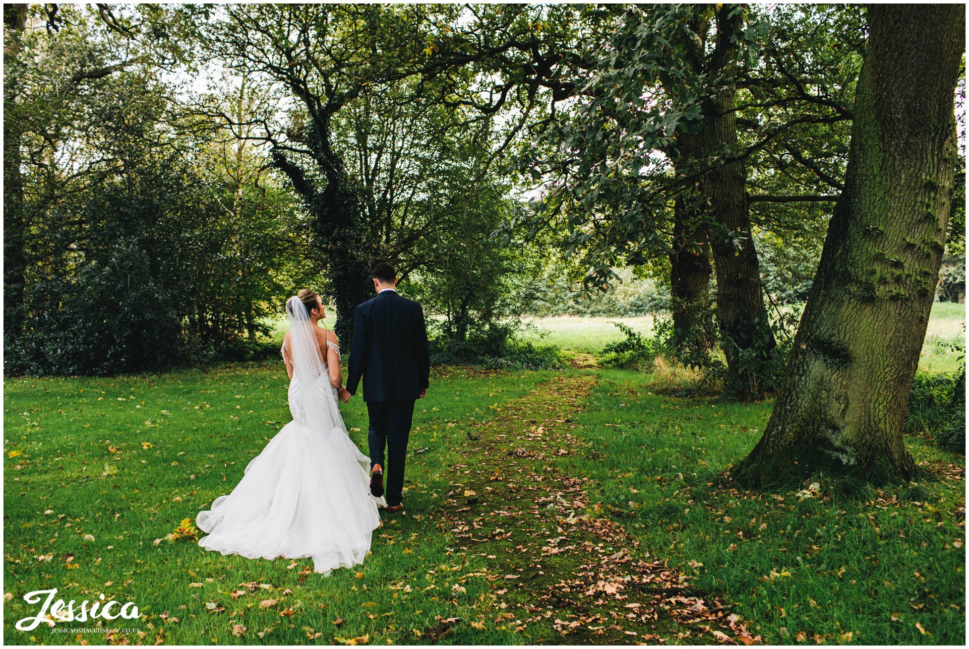 newly wed's walk through the trees in the grounds of their cheshire wedding venue
