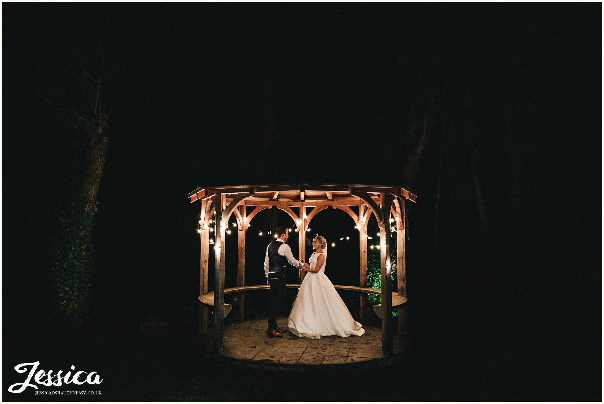 couple stand under festoon lights at their winter wedding