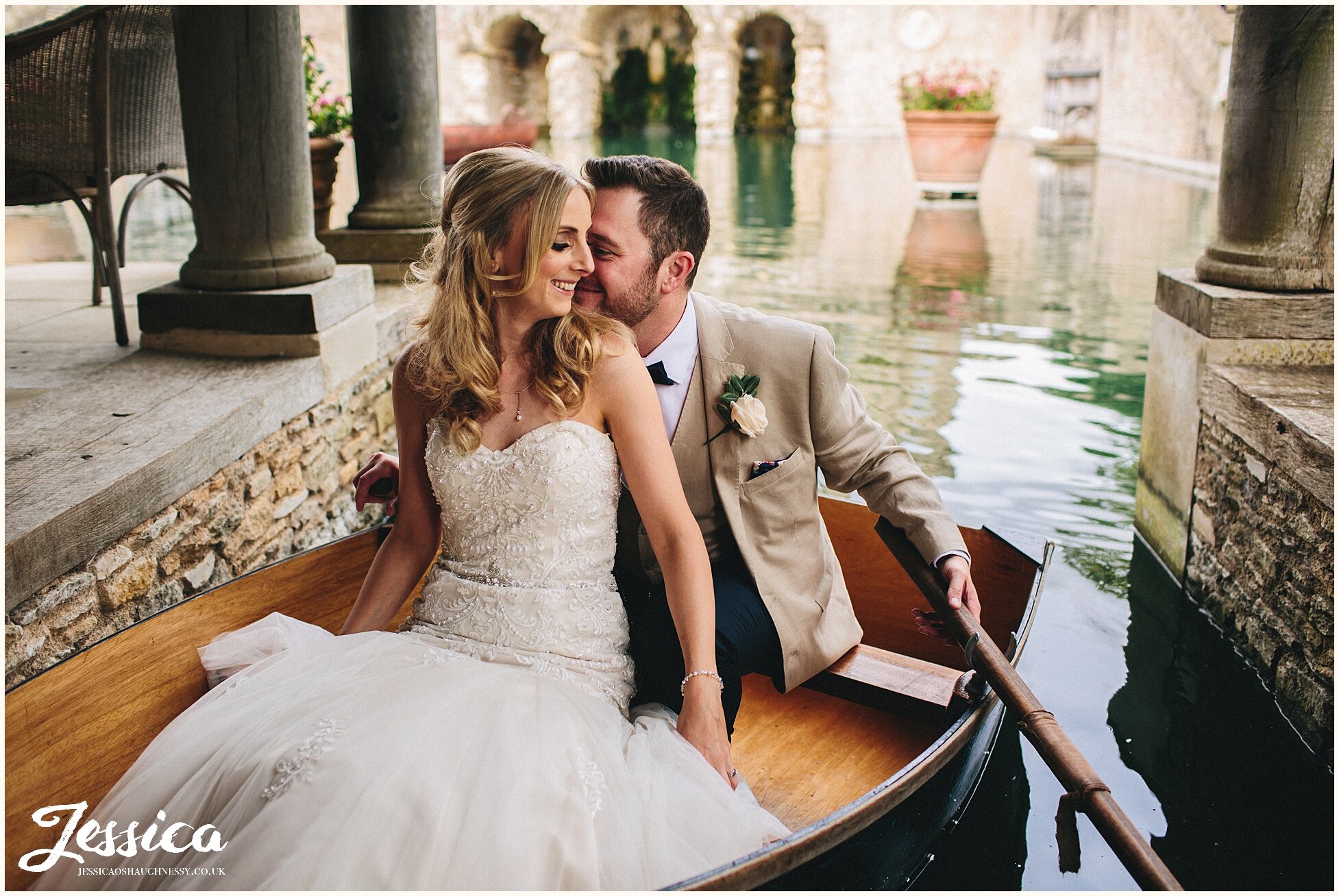 newly wed's sit in wooden boat at the lost orangery in the cotswolds