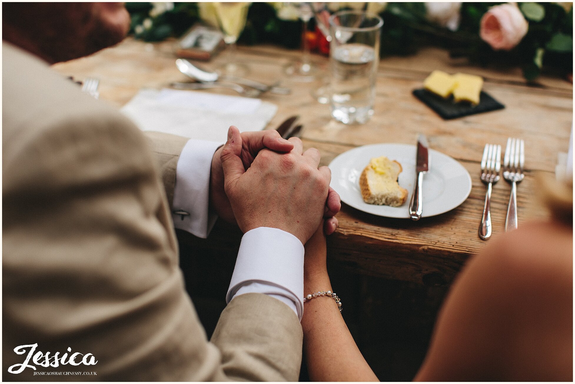 cotswolds wedding photography - bride &amp; groom hold hands on the wedding table