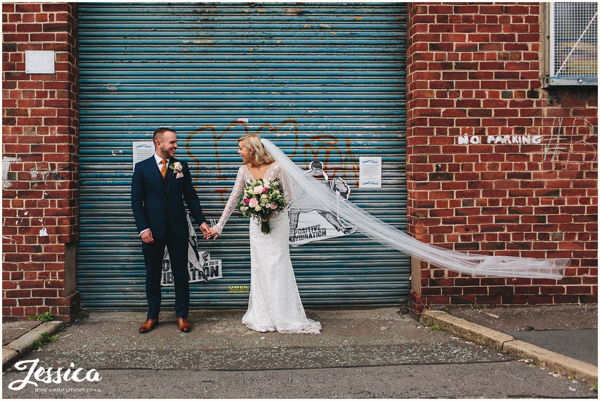 newly wed's hold hands in front of blue urban doorway