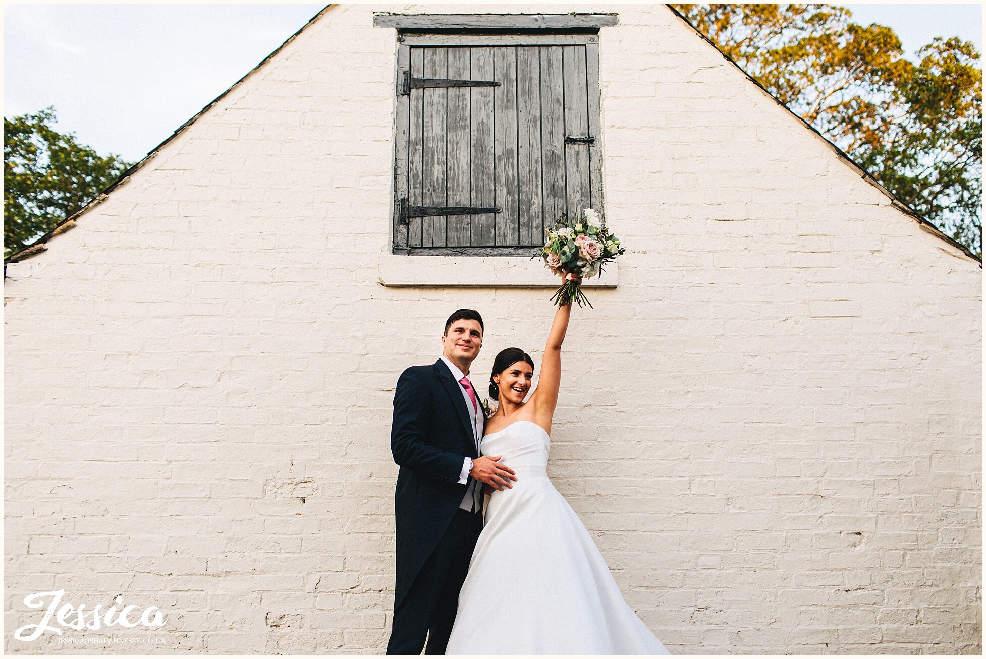 bride waves her bouquet in the air outside the barn in leicestershire