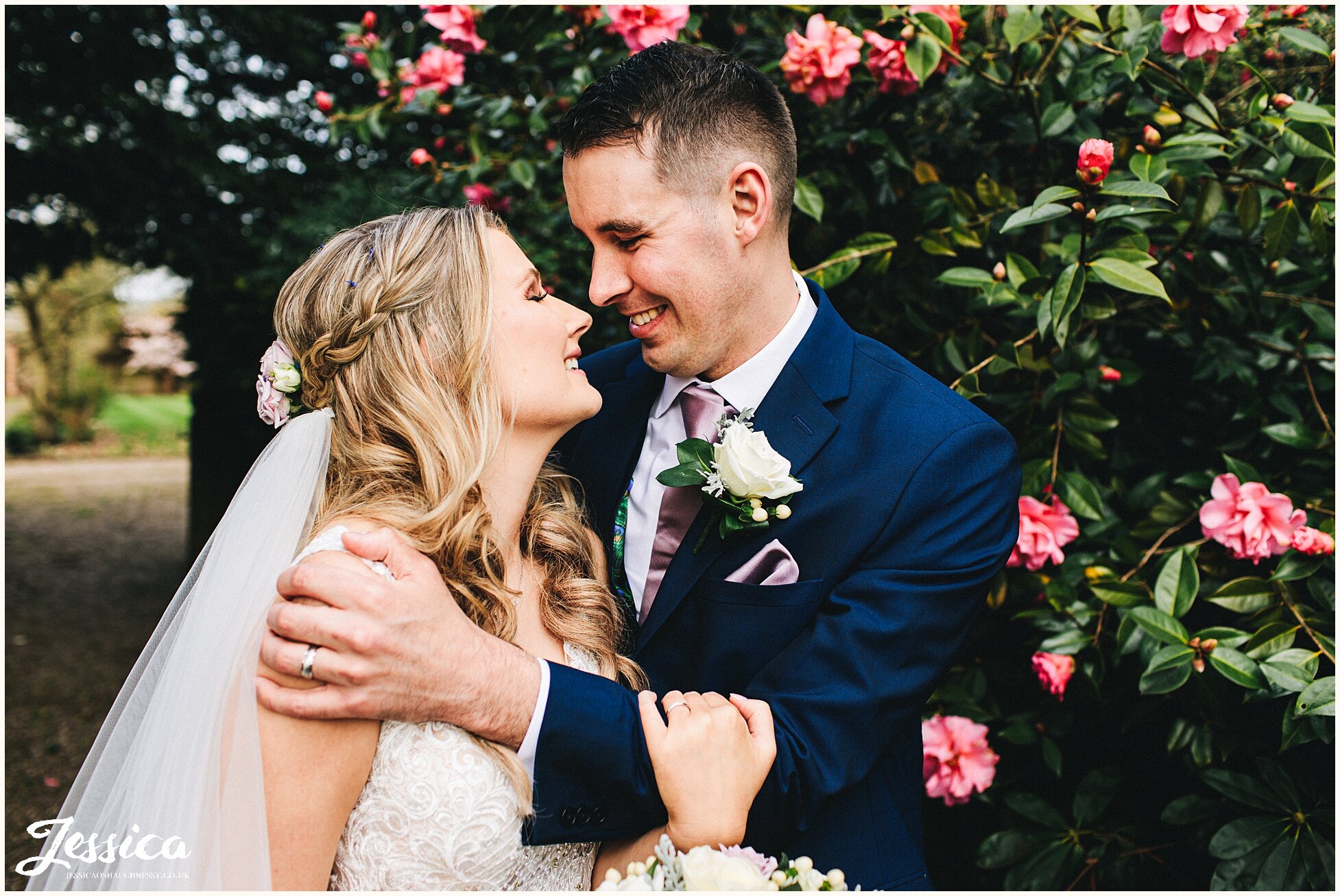 newly wed's hold each other amongst pink flowers at spring wedding