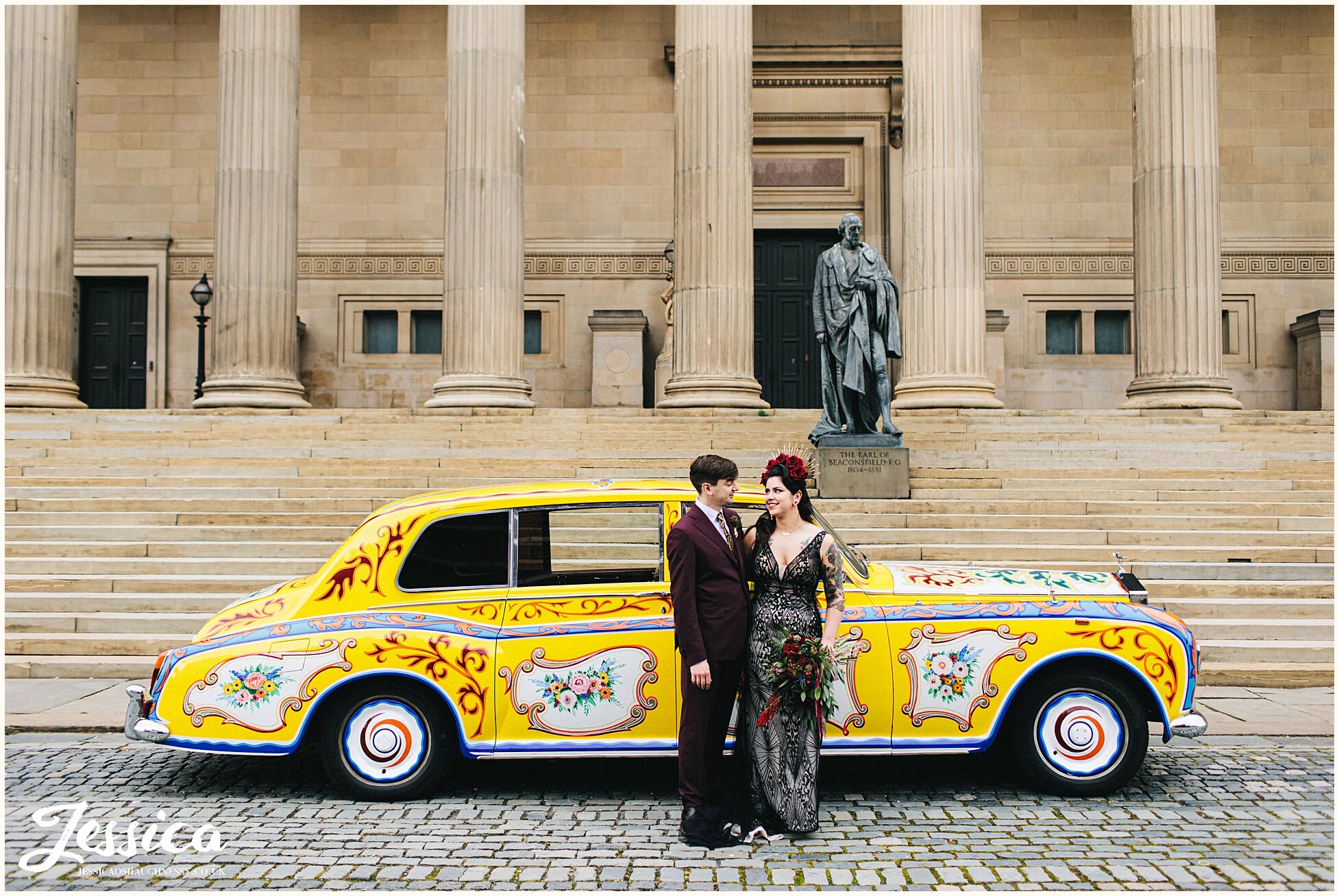 couple pose in front of brightly coloured wedding car