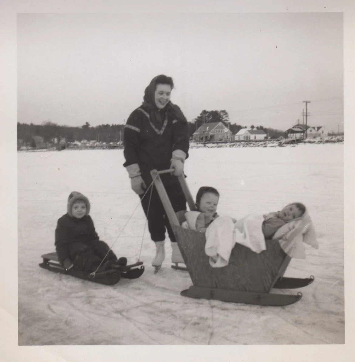 December 1953, Long Lake in Naples, Maine. My father made the plywood sleigh that my mother is pushing with my younger sister and I aboard. My older sister on the sled behind. - James