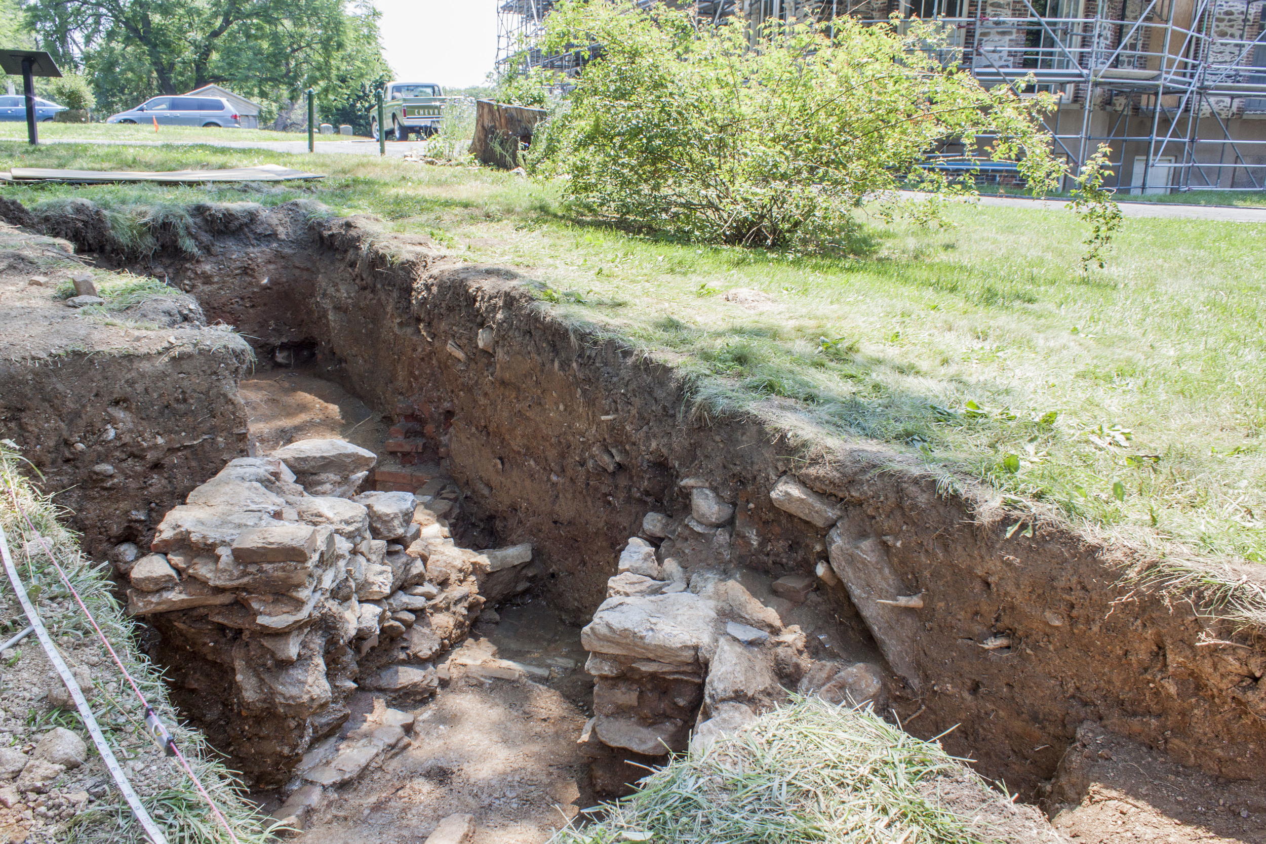 The first excavation trench, facing southeast towards the mansion, shows rough schist walls flanking the subterranean path. 