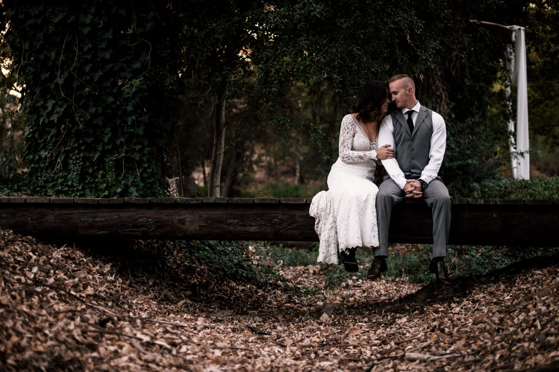 bride and groom sit on rustic bridge at rustic pymm ranch wedding venue in winchester california