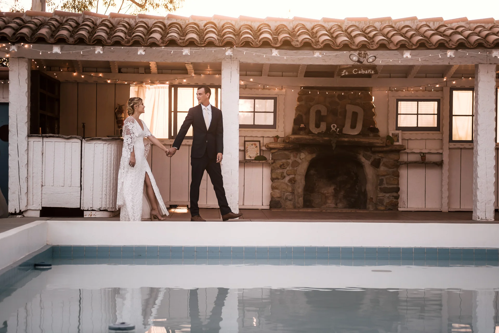 groom leads his bride past the pool captured by photographer during romantic wedding at the historic Leo Carrillo Ranch in Carlsbad California