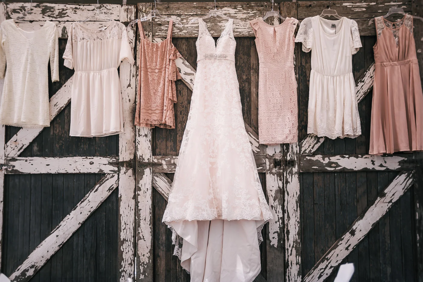 Brides beautiful dress hangs on a set of barn doors alongside her bridesmaids dresses.