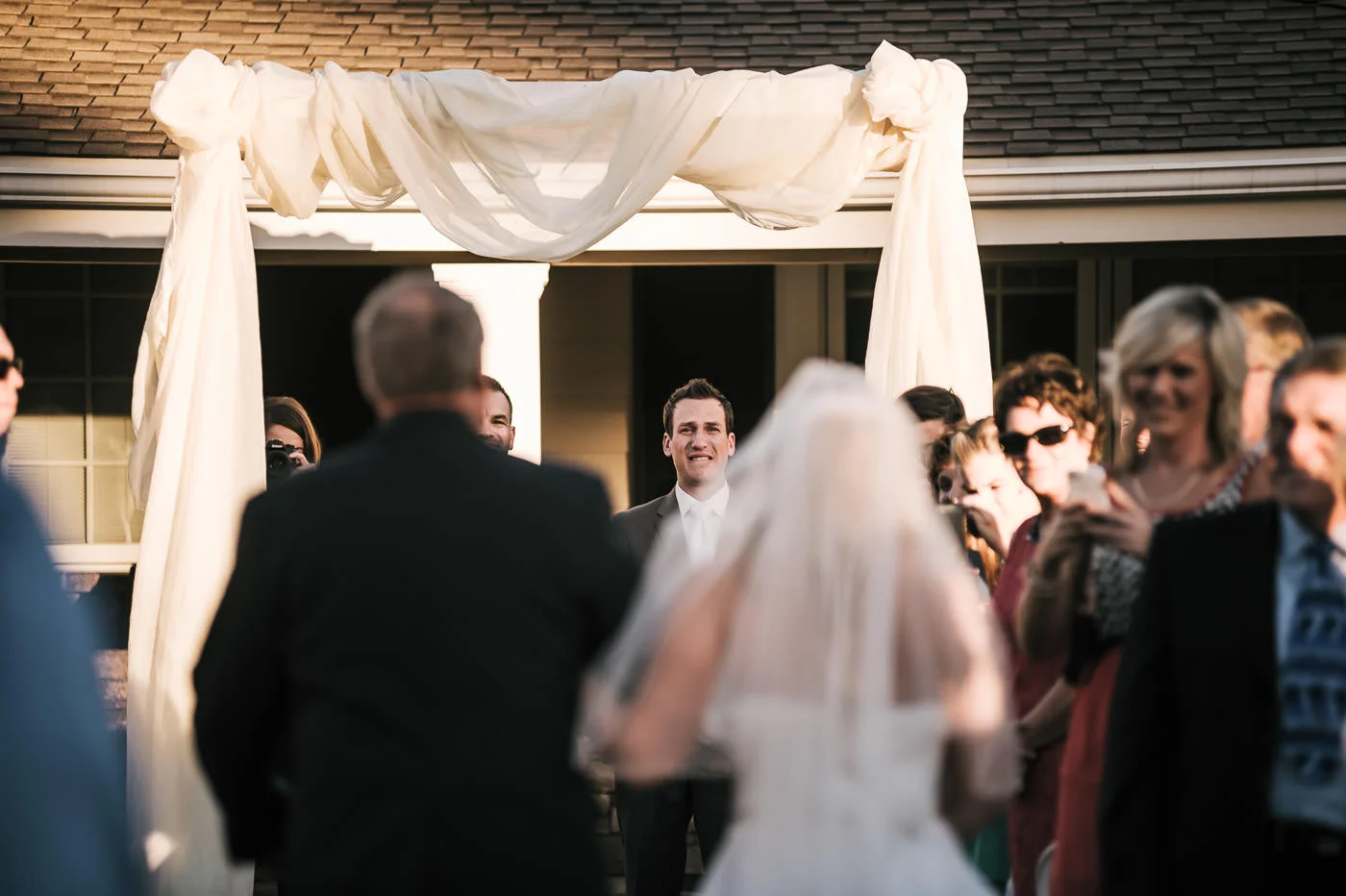 Groom sheds tears of joy as he sees his bride coming down the aisle at their backyard marriage ceremony.